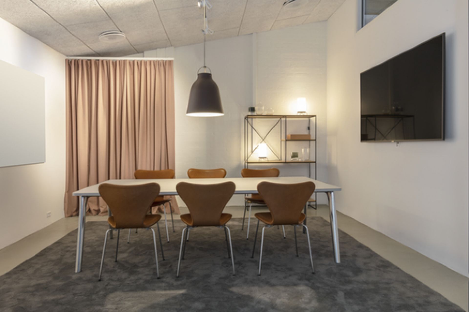 Innenraum mit Fritz Hansen Planner Regal, Esstisch, Stühlen und TV-Gerät an der Wand.