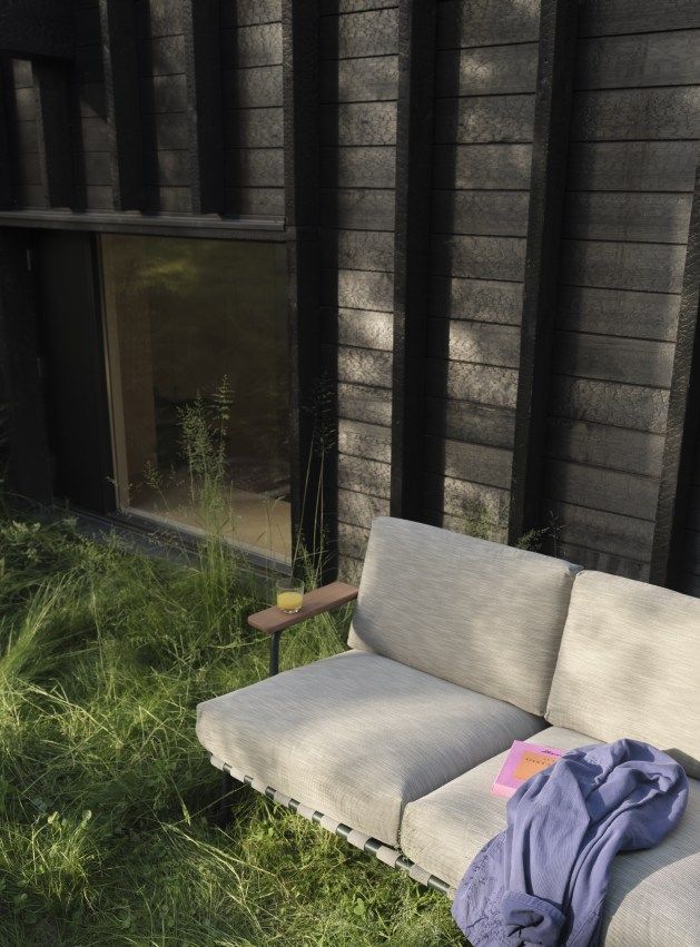 Muuto Settle Outdoor Sofa 2-Sitzer in Beige mit Getränk und Buch im Garten.