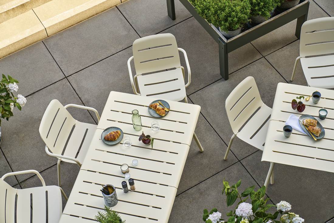 Weishäupl Vapio Stuhl Outdoor: Beige Gartenstühle und Tische aus Metall auf einer Terrasse mit Speisen.