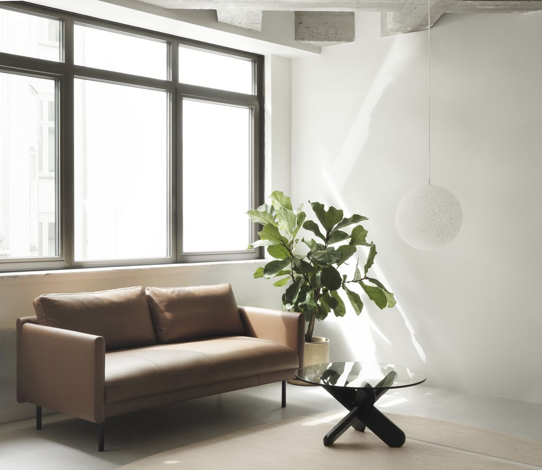 Normann Copenhagen Rar Sofa 2-Sitzer in braunem Leder, modernes Wohnzimmerambiente mit Pflanze, Lampe und Beistelltisch.