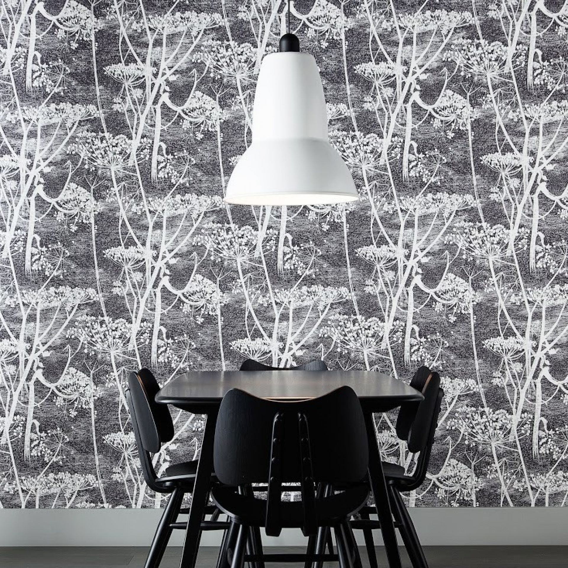 Weiße Anglepoise Original 1227 Giant Pendelleuchte über schwarzem Esstisch mit Stühlen vor gemusterter Tapete.