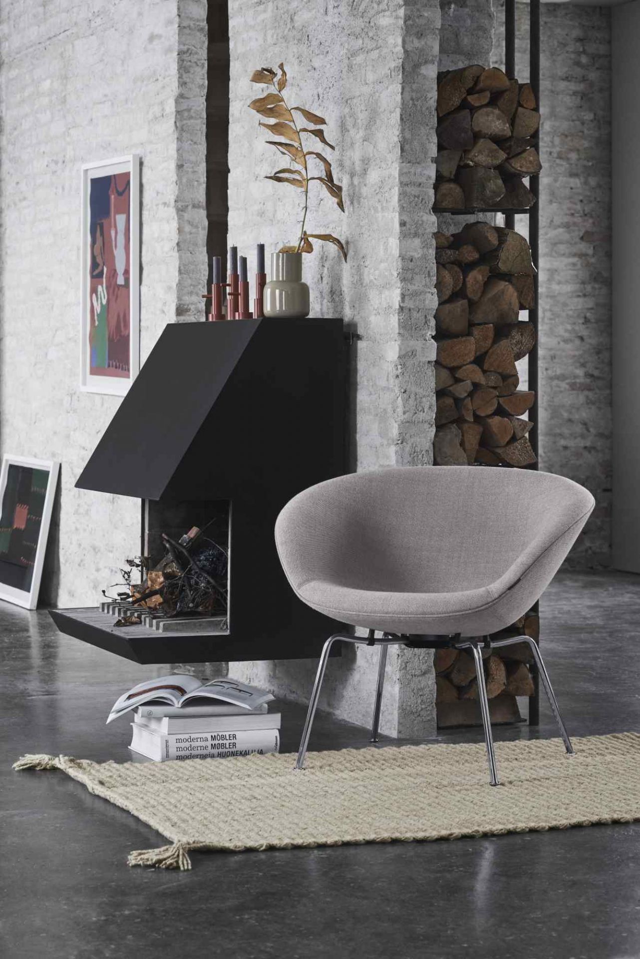 Grauer Fritz Hansen Pot Sessel mit Stahlbeinen vor Kamin und Brennholzregal in modernem Wohnzimmer.