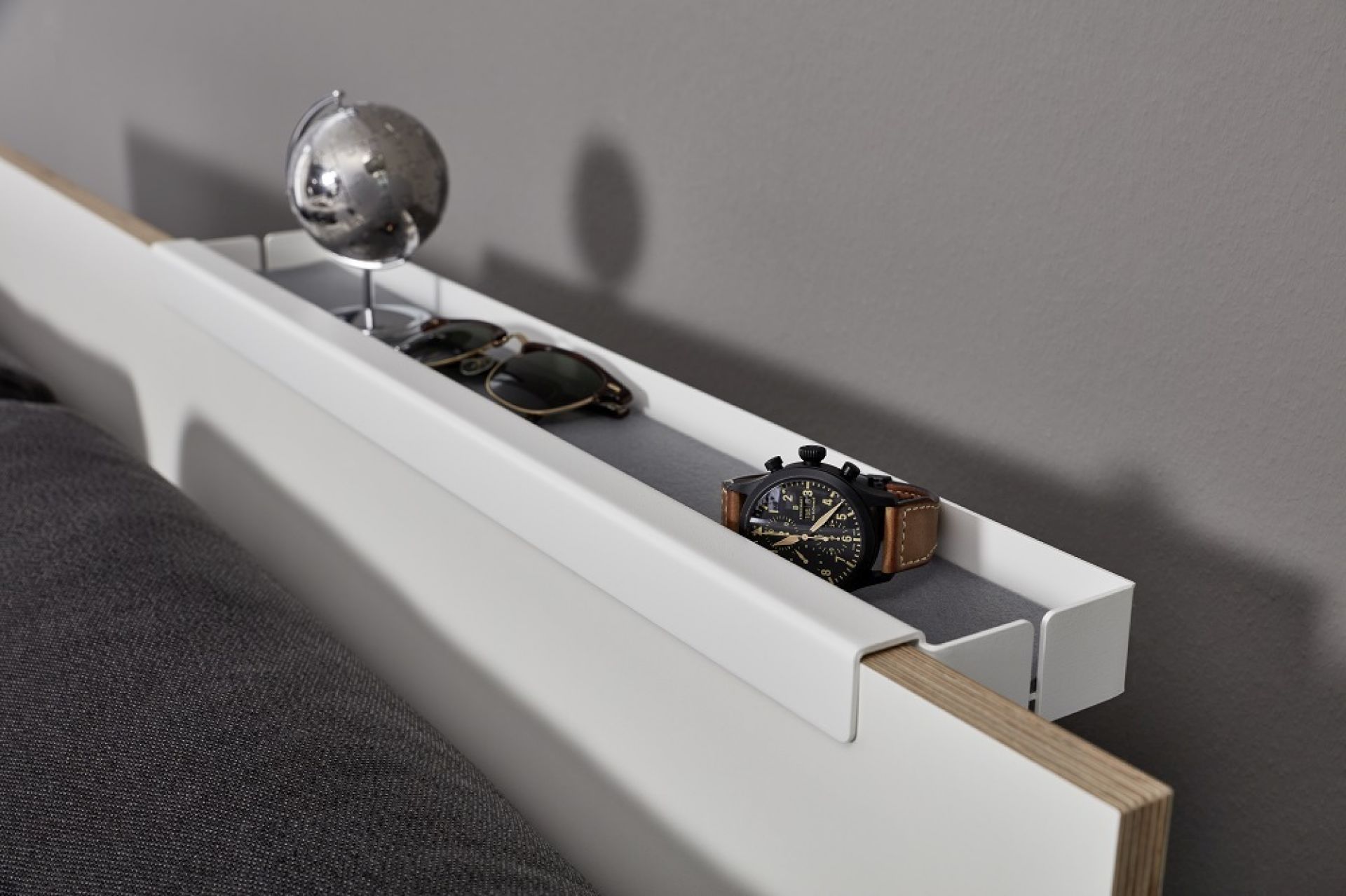 Flai Einzelbett von Müller Möbelwerkstätten mit Ablage für Uhr, Globus und Sonnenbrille.