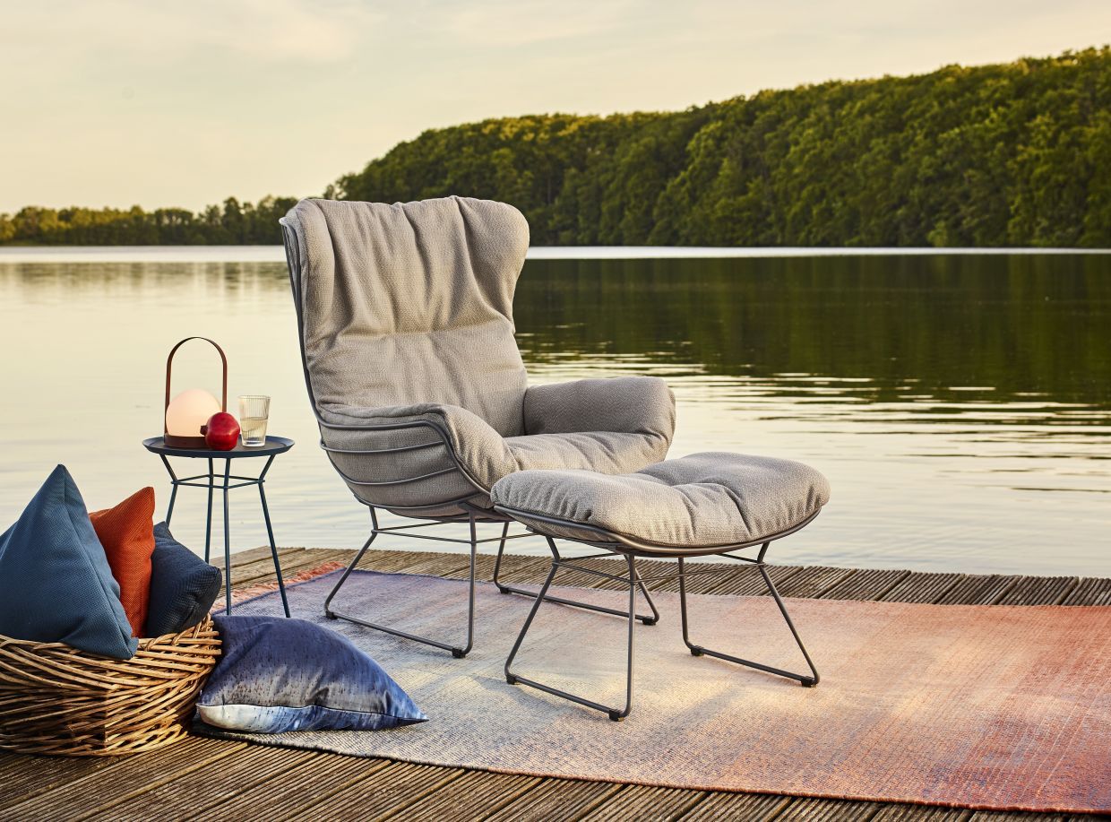 Leyasol Ottoman Outdoor von Freifrau Manufaktur, grauer Sessel mit Hocker auf Holzsteg am See.
