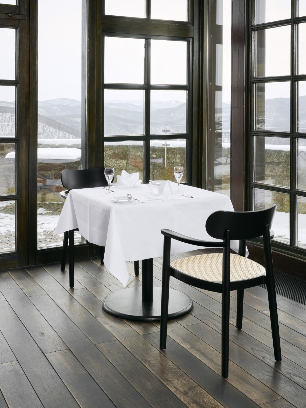 Schwarzer Holzstuhl 118 FV Thonet mit Armlehnen und Wiener Geflecht am Esstisch in modernem Restaurant.