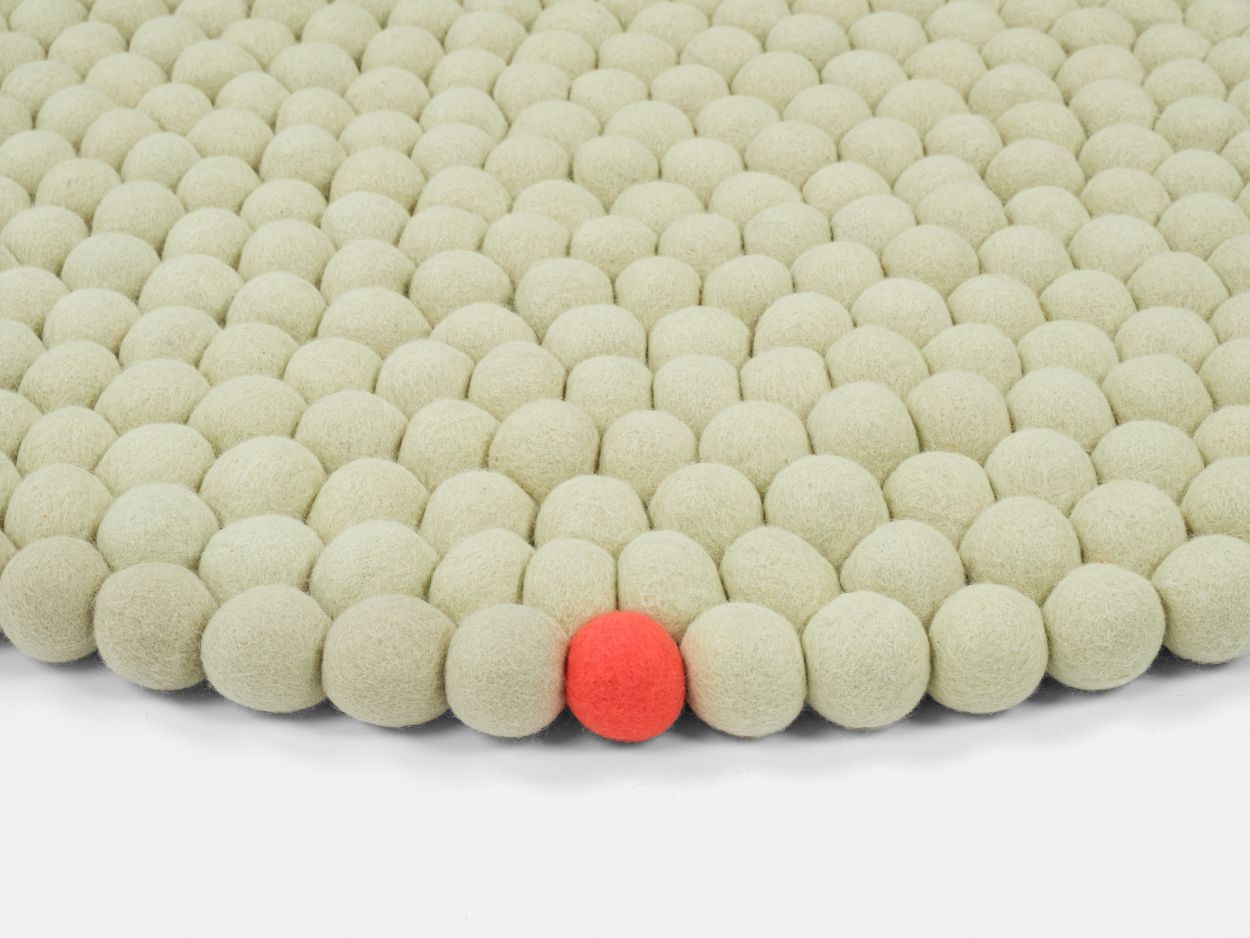 Detailaufnahme des Big One Filzteppichs in Grünbeige, bestehend aus vielen Filzkugeln, mit einer roten Kugel.