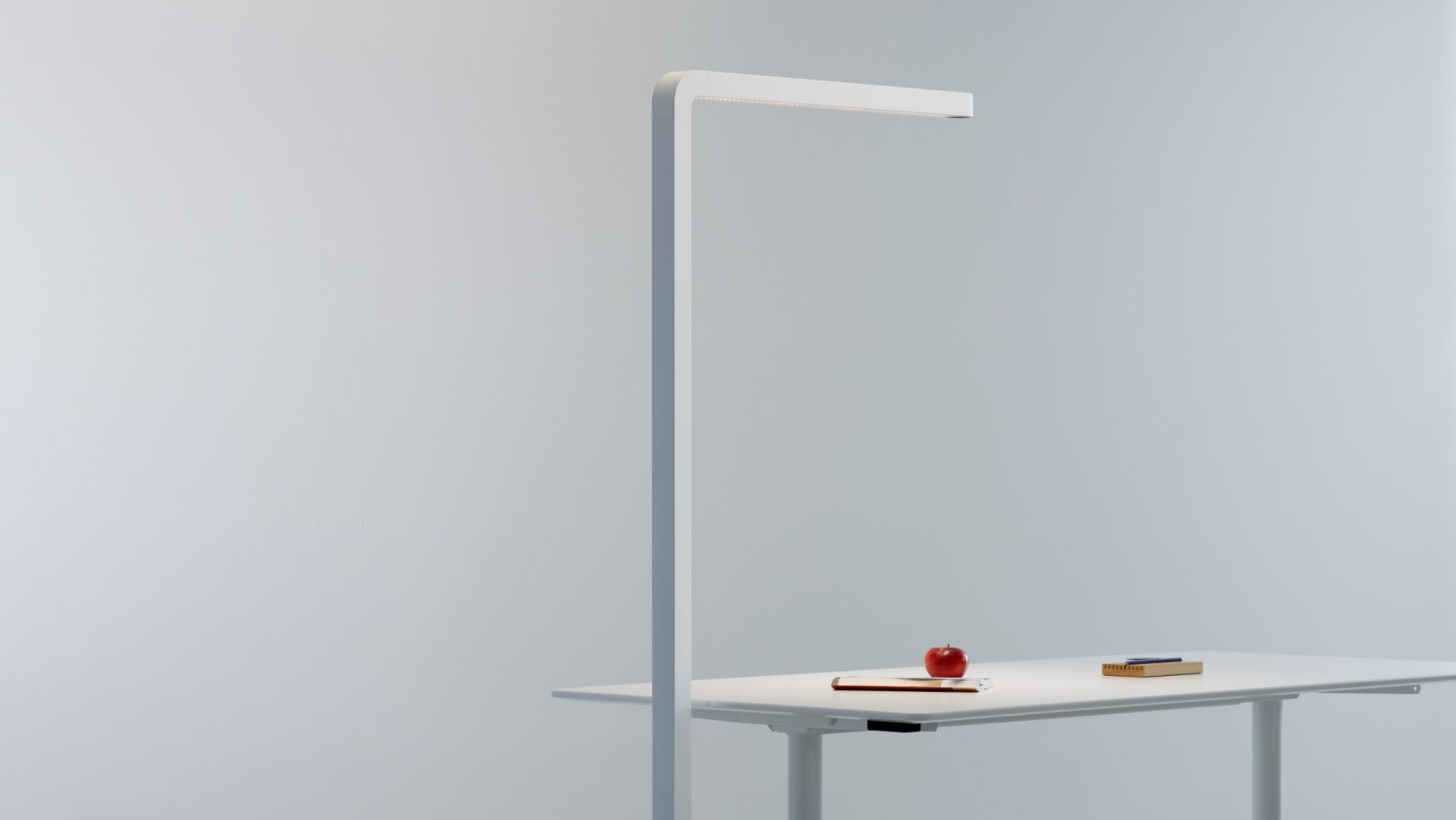 Team Agile Stehleuchte in Grau über einem Schreibtisch mit Apfel, Notizbuch und Stifthalter.