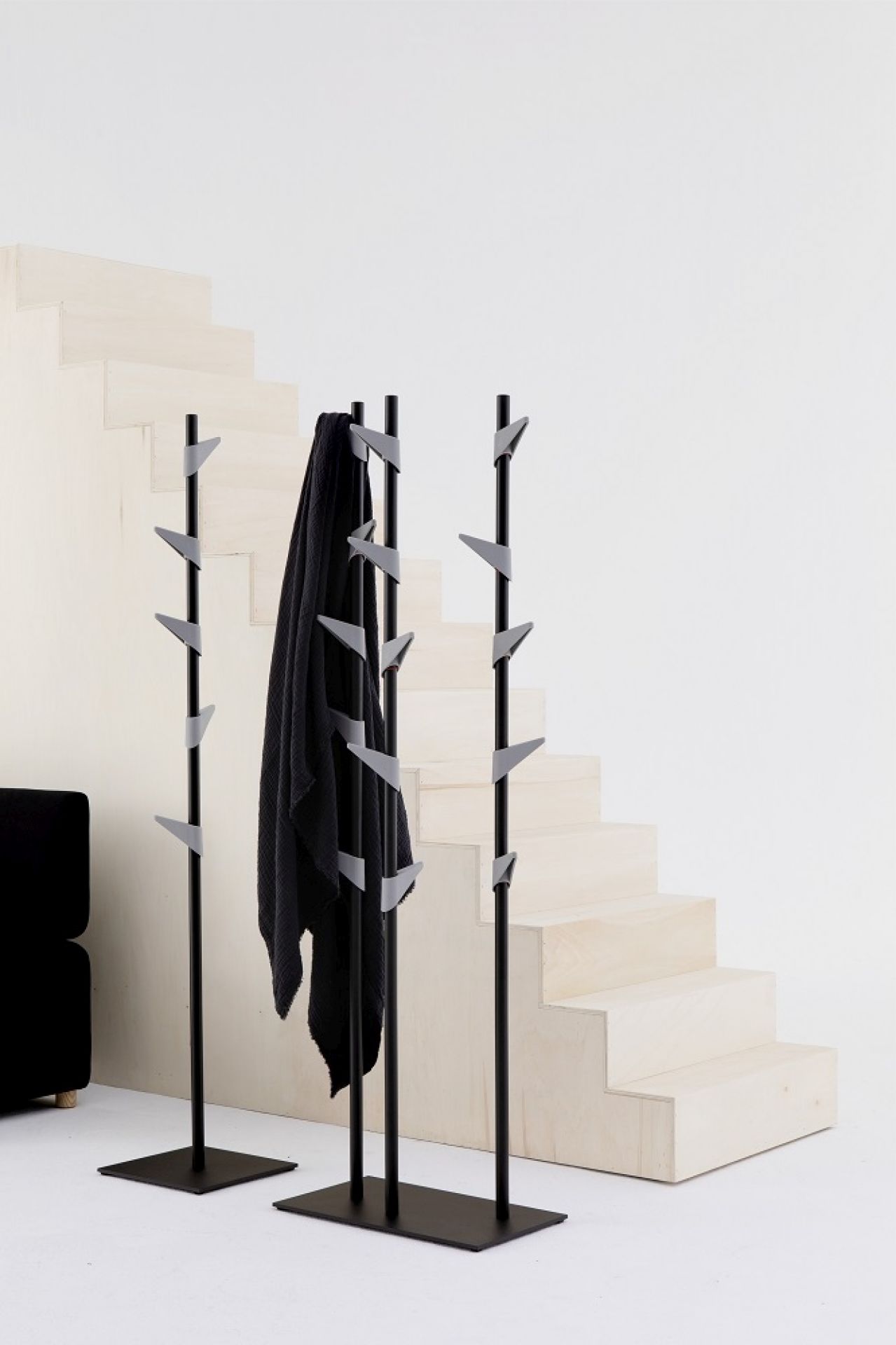Cascando Standgarderobe aus Bambus mit schwarzem Mantel vor einer hellen Treppe im minimalistischen Design.