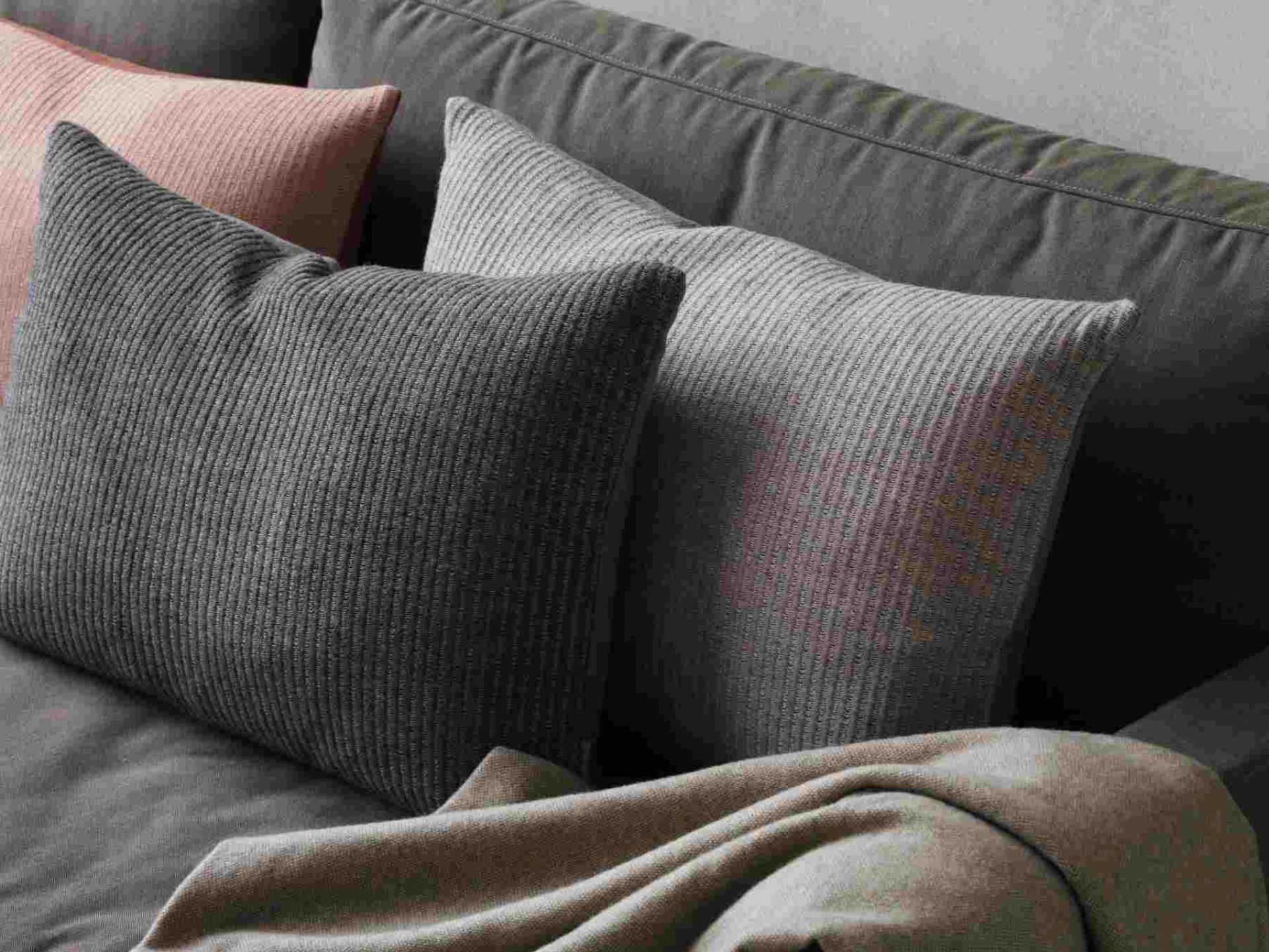 Detailaufnahme des Fritz Hansen Lissoni Sofas mit Kissen und Decke in Grautönen.
