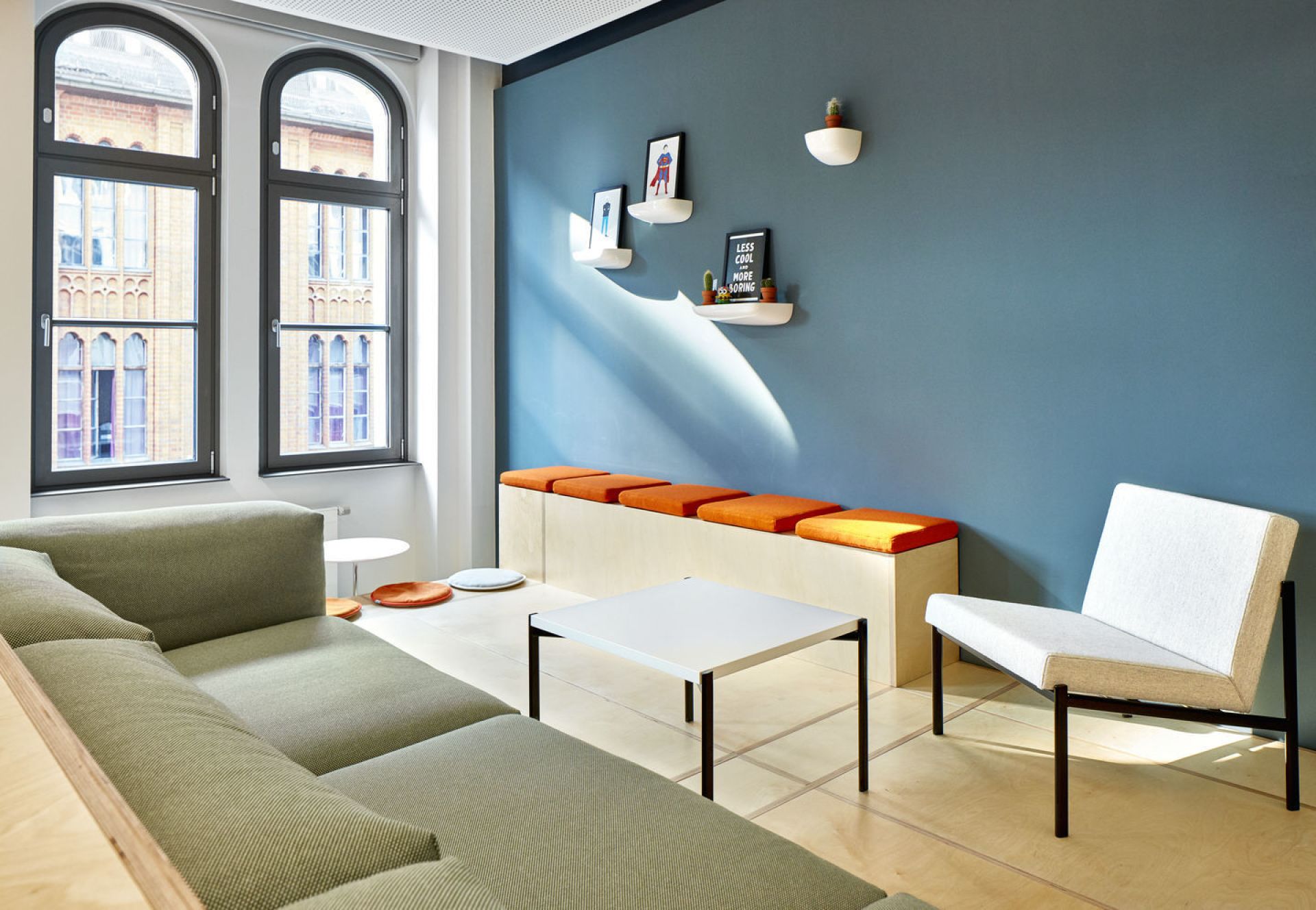 Helle Büroeinrichtung mit Vitra Corniches Wandboards an blauer Wand, Sofas, Tisch und Stuhl.