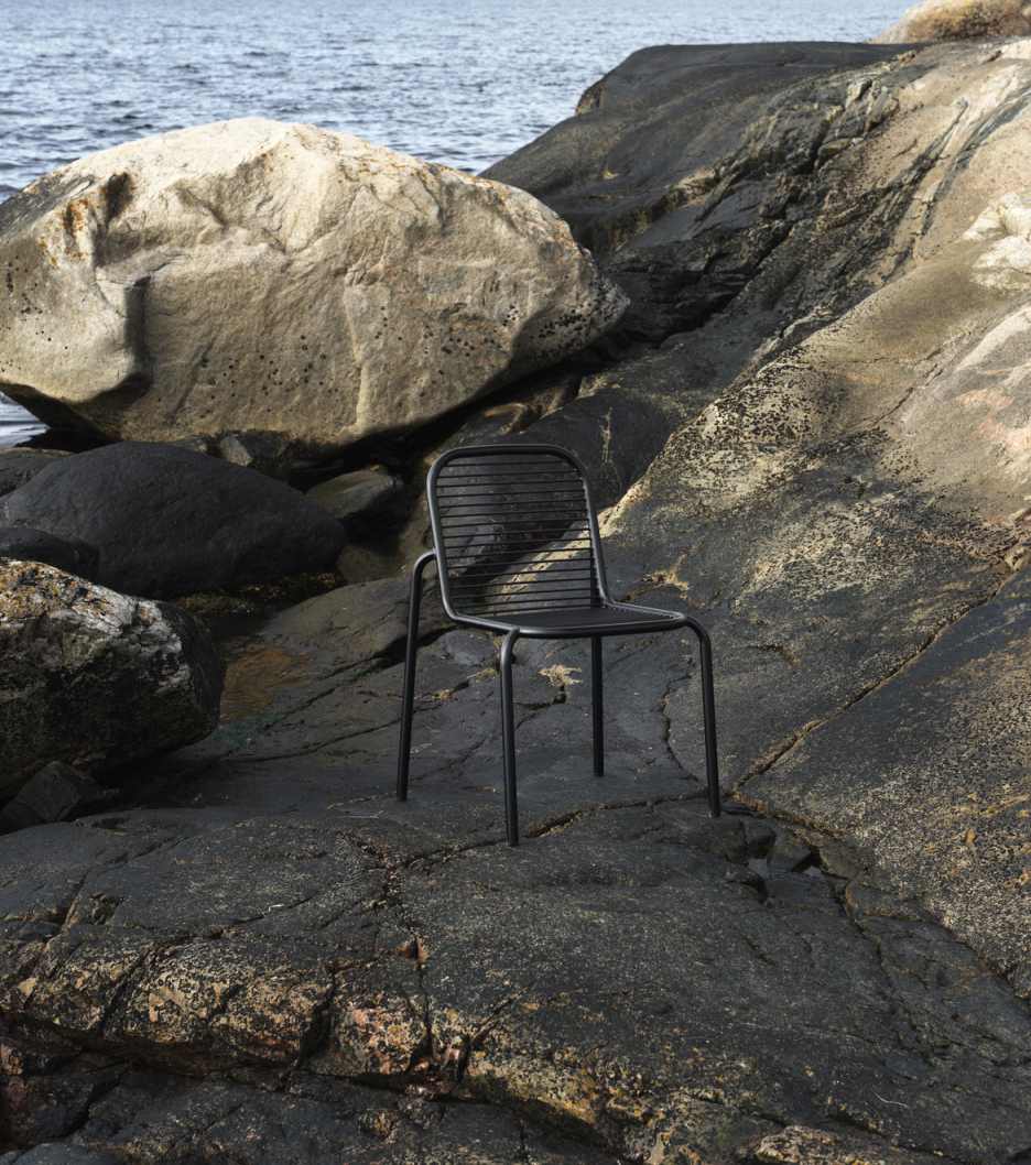 Schwarzer Vig Chair Stuhl von Normann Copenhagen auf felsigem Untergrund im Freien, Meer im Hintergrund.