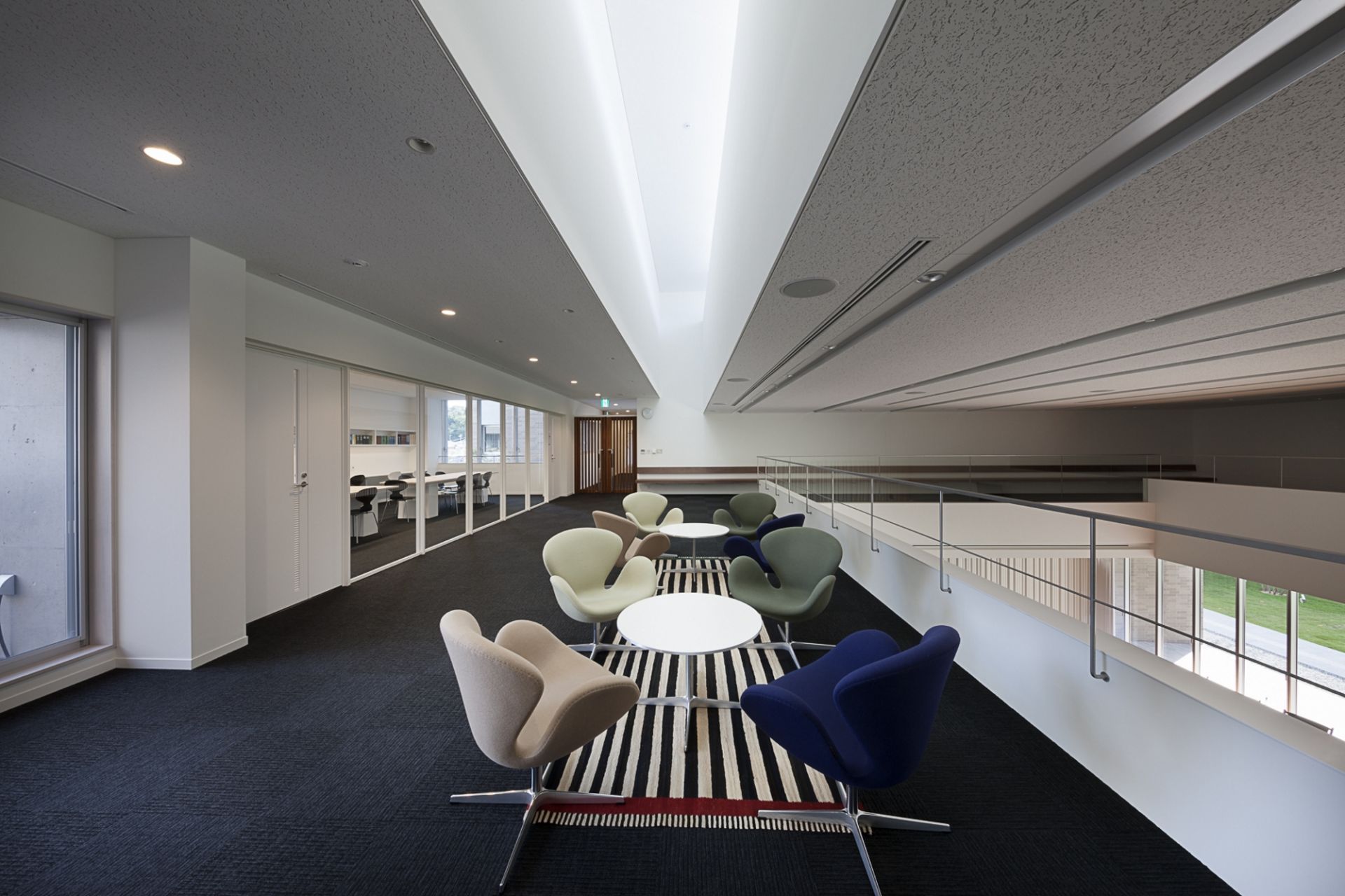 Mehrere Fritz Hansen Schwan Sessel in Beige, Blau und Grün um weiße Tische in modernem Büro.