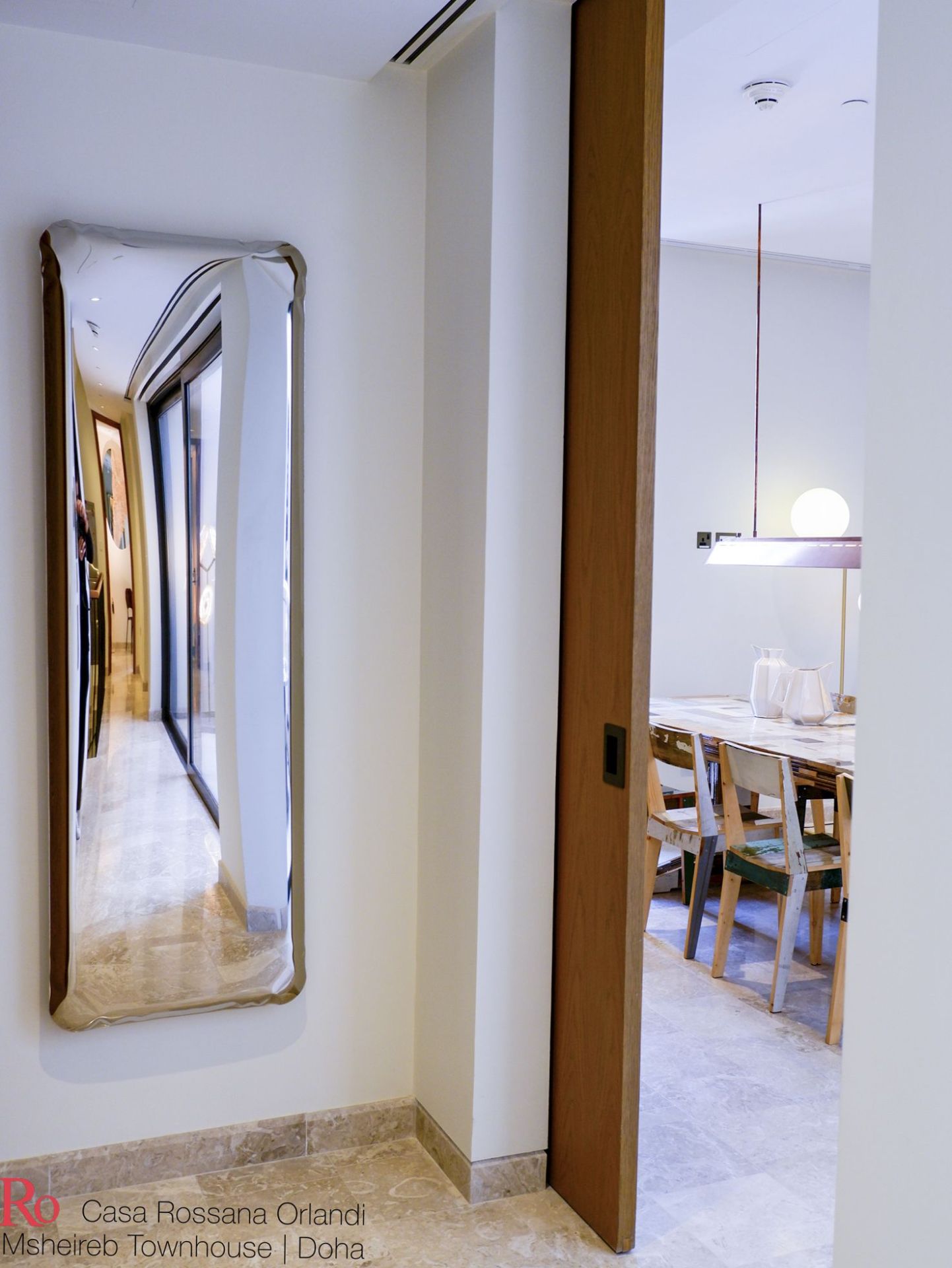 Tafla Q Spiegel von Zieta, ein verzerrtes Designobjekt mit braunem Rahmen an einer weißen Wand.