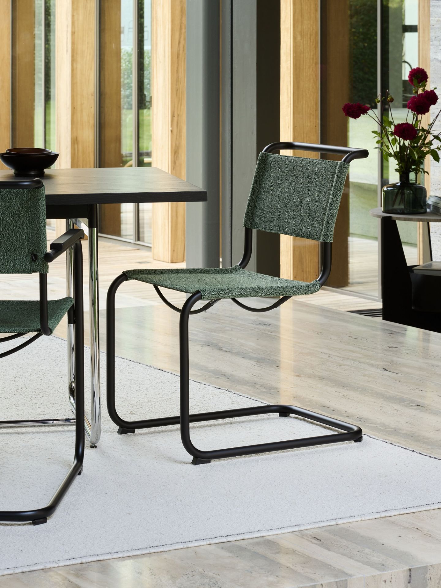 Nahaufnahme eines grünen Thonet S 33 Freischwinger Stuhls mit schwarzem Stahlrohrgestell im modernen Esszimmer.