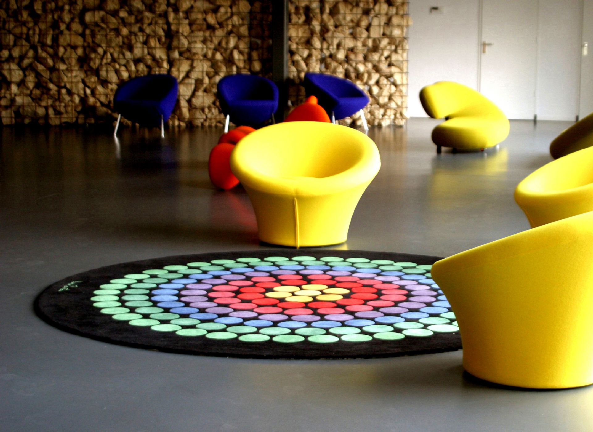 Blick auf einen Panton Teppich mit bunten Kreisen und gelben Designermöbeln.