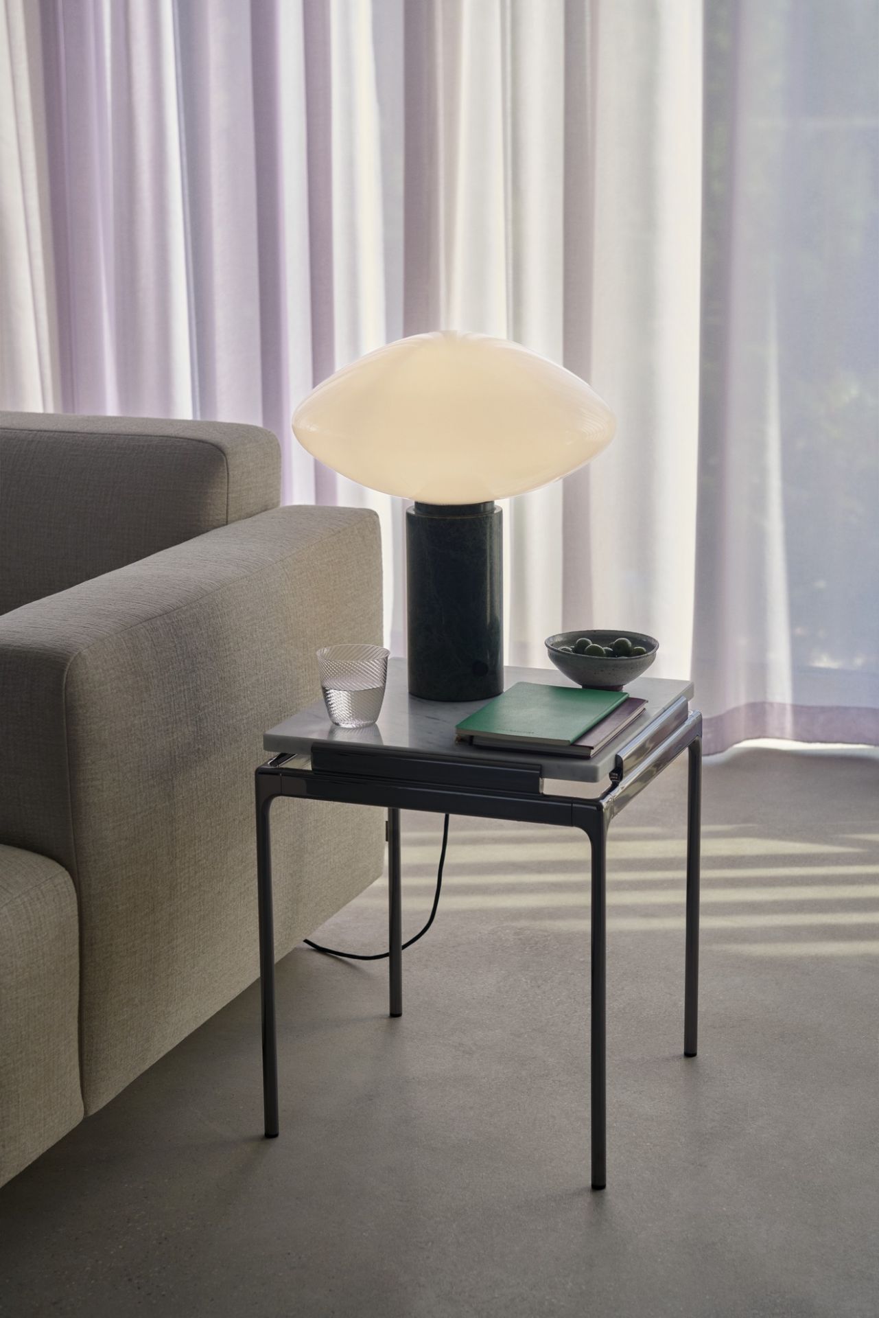 AndTradition Sett LN11 Beistelltisch: Marmor Tischplatte mit Lampe, Glas und Schale neben einem Sofa.