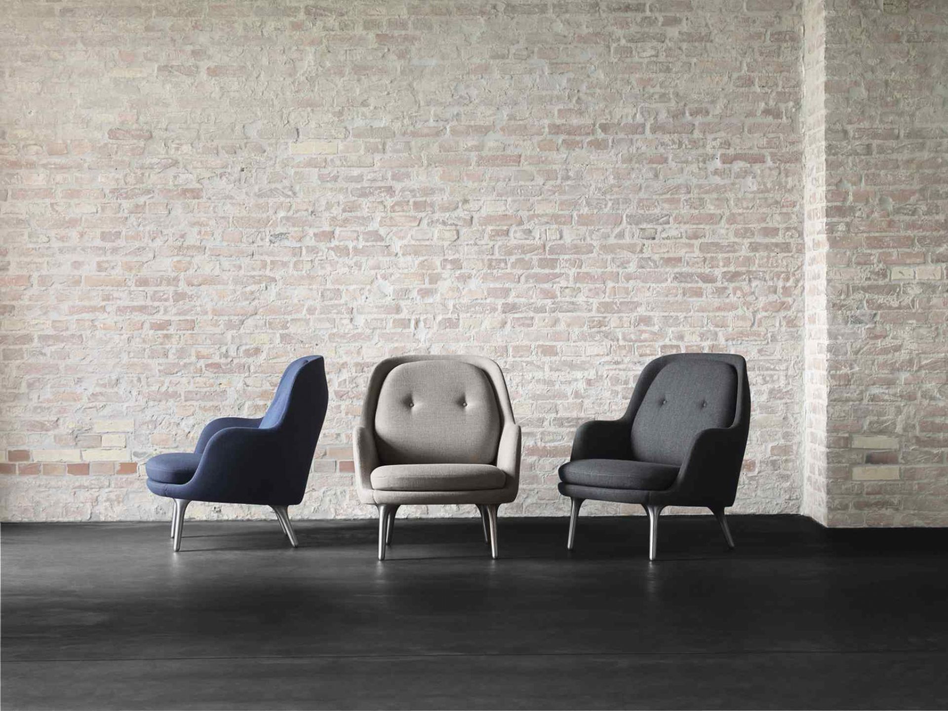 Drei Fri Sessel von Fritz Hansen in Blau, Grau und Anthrazit vor einer Backsteinwand.