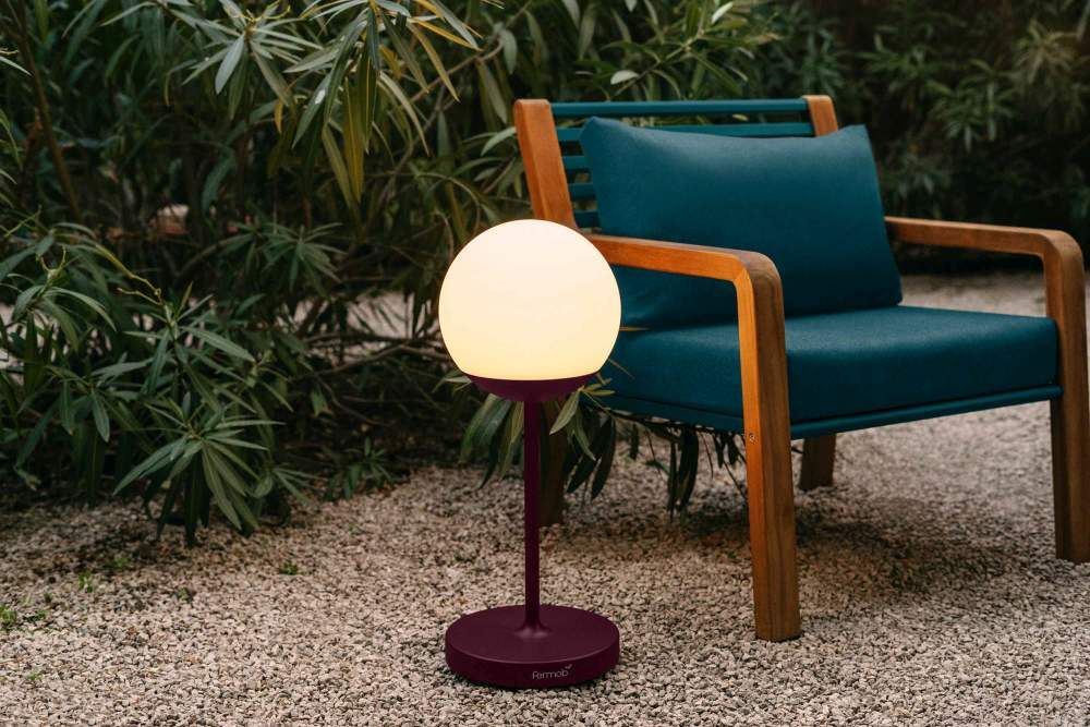 Nahaufnahme des Fermob Somerset Sessels im Freien mit passender Lampe auf Kiesboden.