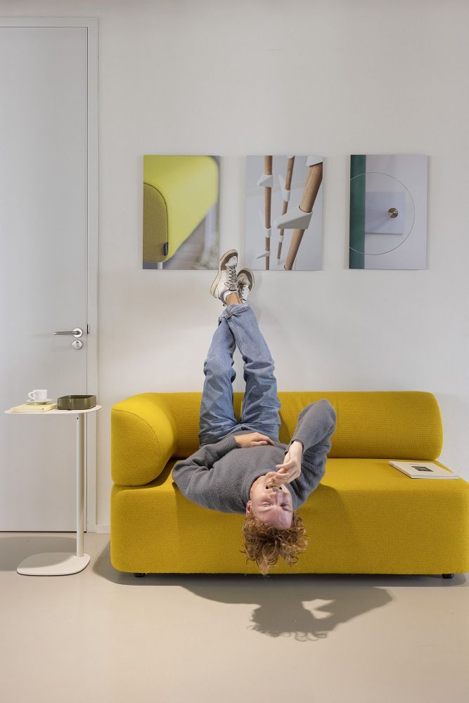 Mann liegt entspannt auf gelbem Mezza Sitzelement Sofa von Cascando, Füße an der Wand.