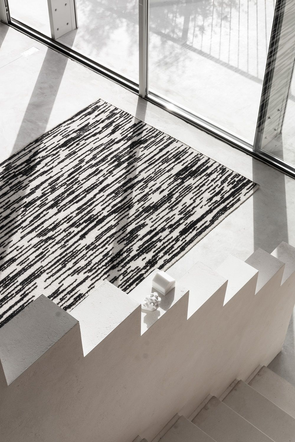 Draufsicht des Nanimarquina Doblecara Rug Teppichs mit abstraktem, schwarz-weißem Muster neben einer Treppe.