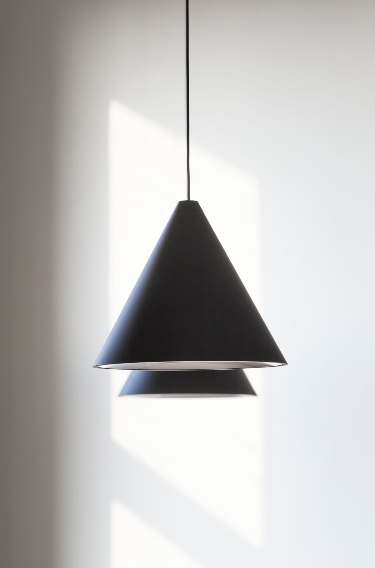 Schwarze Flos String Light Cone Head Pendelleuchte mit kegelförmigem Lampenschirm vor einer weißen Wand.