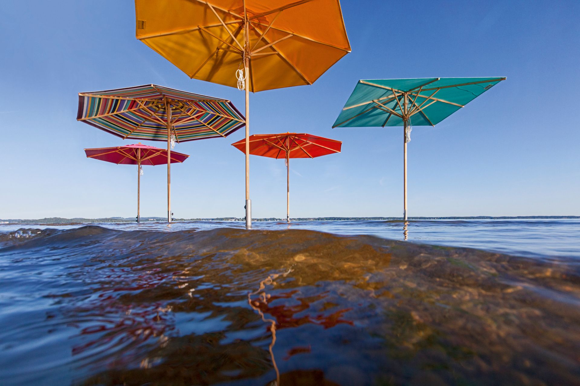 Mehrere bunte Sonnenschirme im Wasser, befestigt mit Bodenhülsen. Sonnenschutz und Schatten.