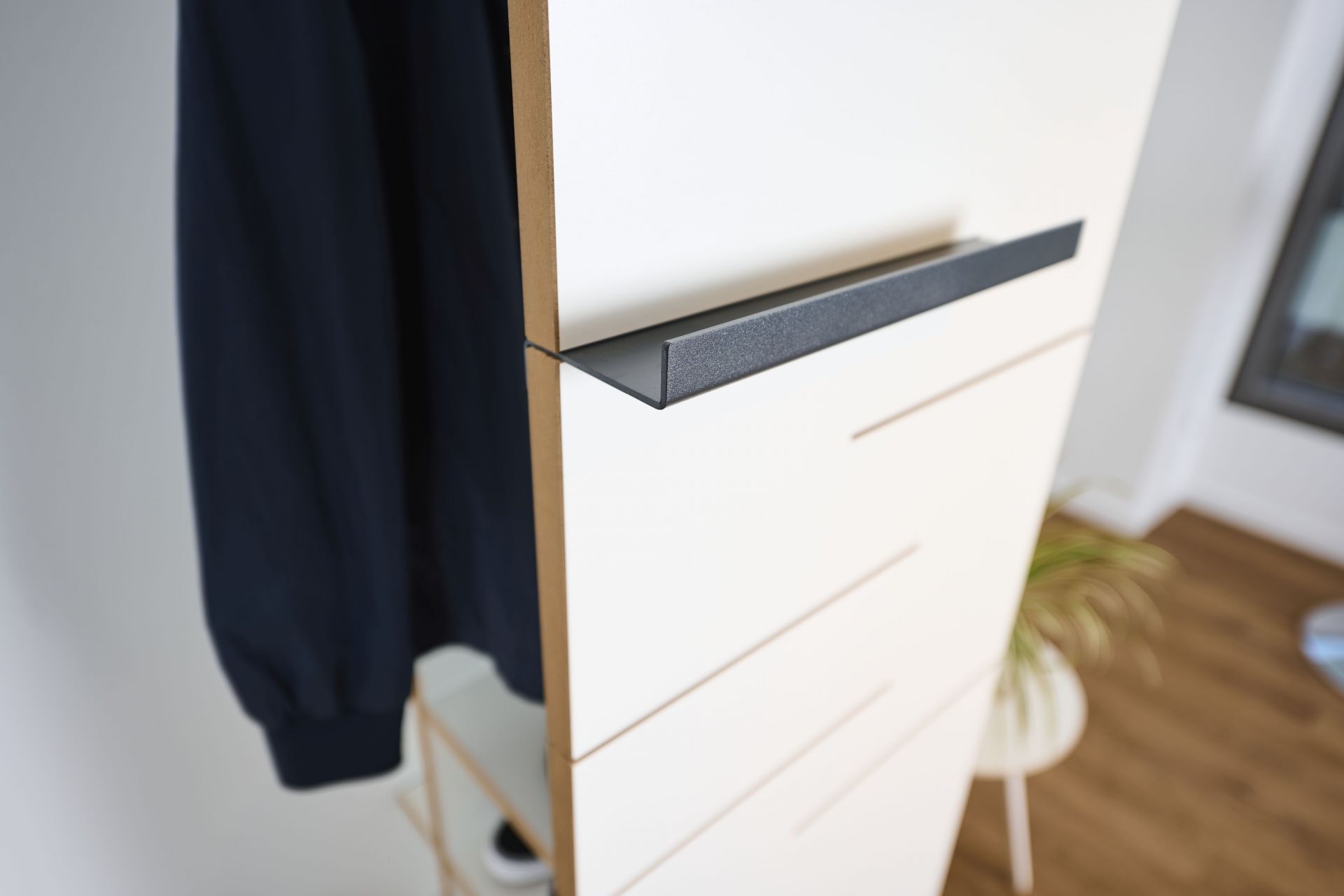 Detailaufnahme der Tojo Ablage: Modernes Wandregal mit schwarzer Ablage und hängender Jacke.