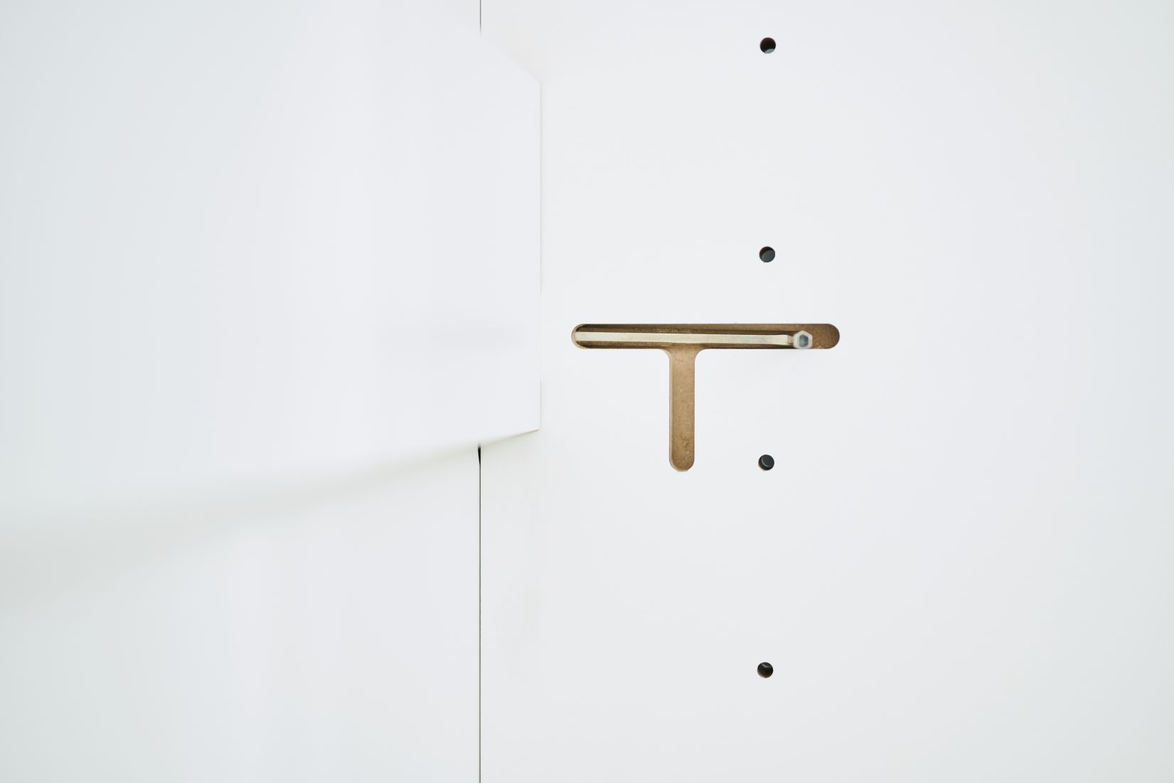 Detailaufnahme des Tojo Schrank Grundmoduls: Weiße Schrankwand mit T-förmiger Aussparung und Bohrlöchern.