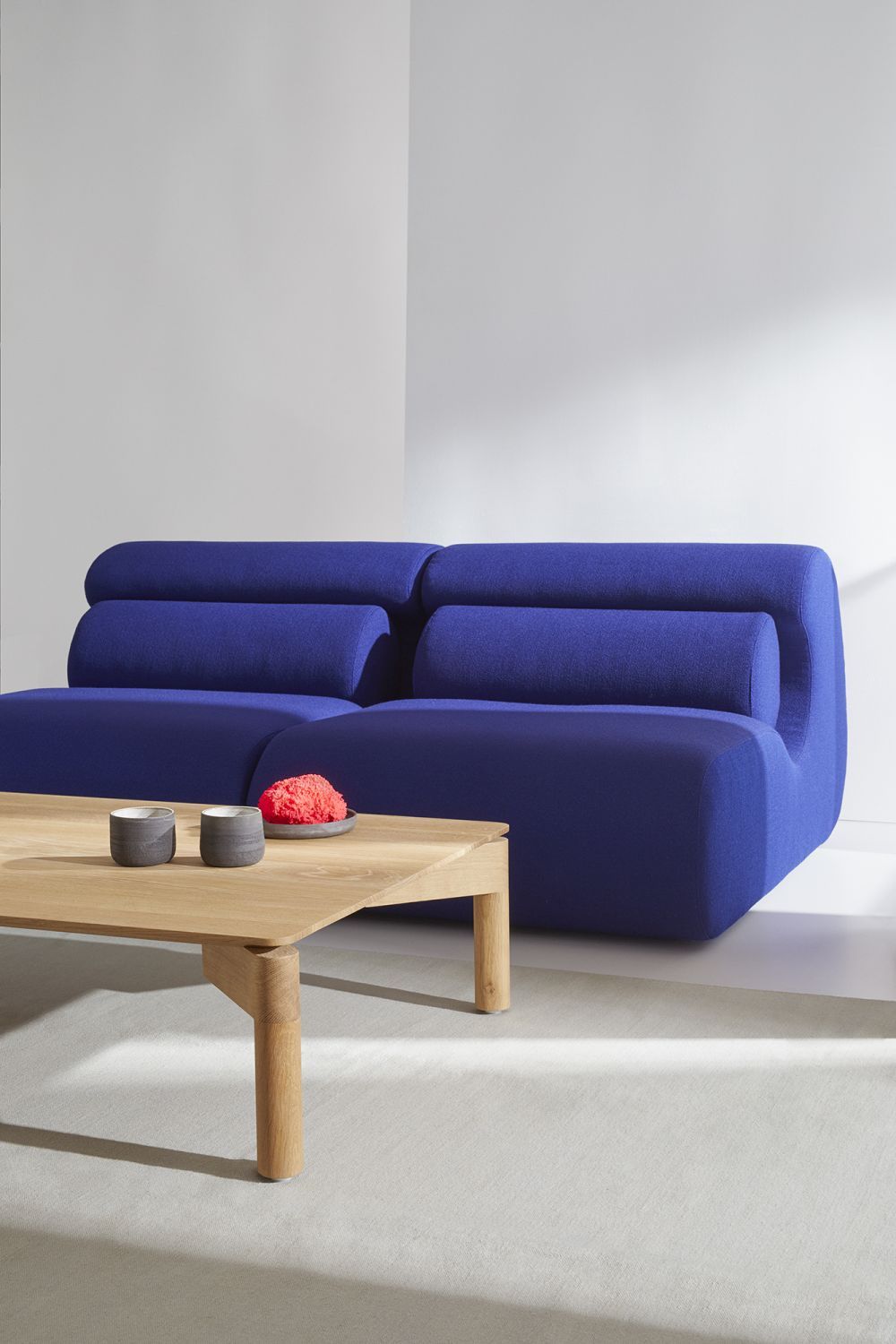 Blaues OLA Sofa mit Pouf und Holztisch im modernen Wohnzimmer, bequeme Sitzgelegenheit.
