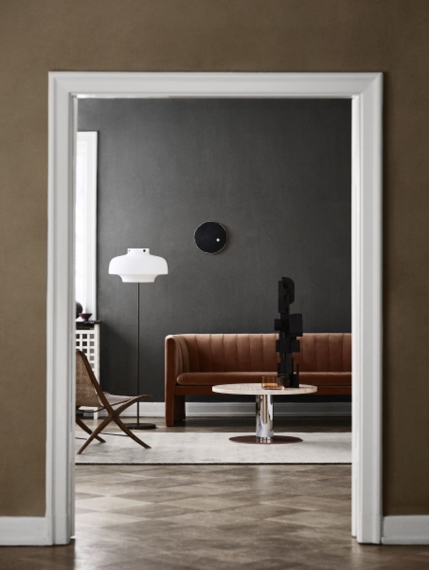 Wohnzimmer mit braunem Sofa, Stehlampe und The Moor Rug Teppich AndTradition in hellem Grau.