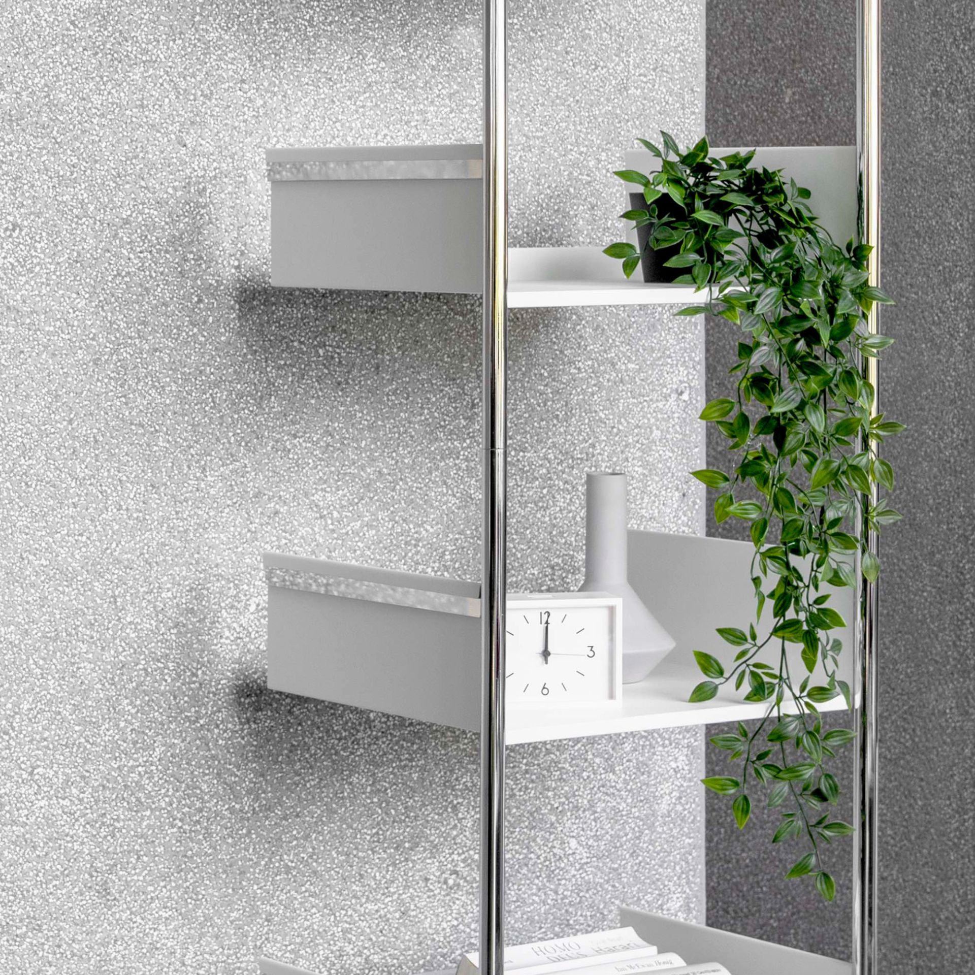 Modernes, weißes Anlehnregal Pool 220 von Mox mit Chromgestell, dekoriert mit Pflanze, Uhr und Wohnaccessoires.