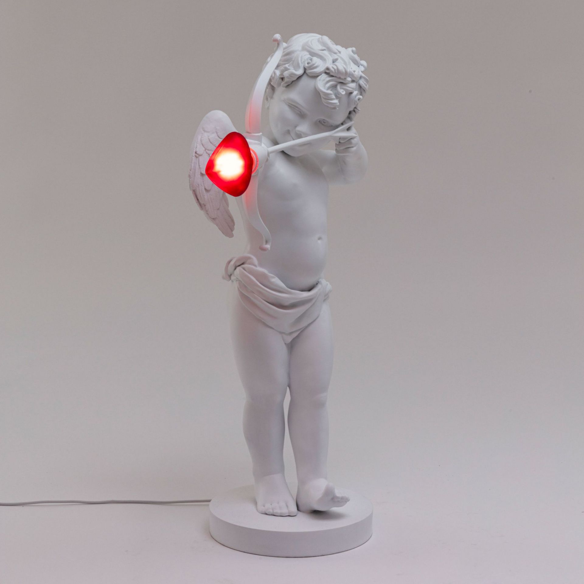 Cupid Lampe von Seletti, weiße Tischleuchte in Form eines Amor mit rotem Herz-Pfeil.