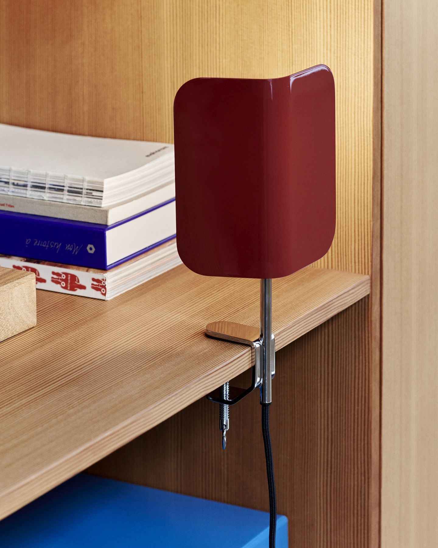Nahaufnahme der roten Hay Apex Clip Lamp Klemmleuchte, befestigt an einem Holzregal mit Büchern.
