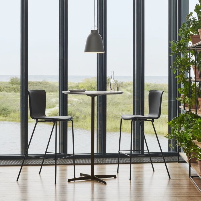 Graue Caravaggio Pendelleuchte von Fritz Hansen über einem runden Tisch mit zwei Barhockern in modernem Ambiente.