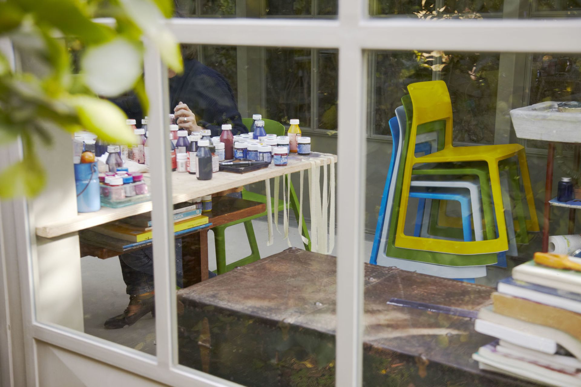 Gestapelte Vitra Tip Ton Stühle aus Kunststoff in Gelb, Grün, Weiß und Blau hinter Fenster.