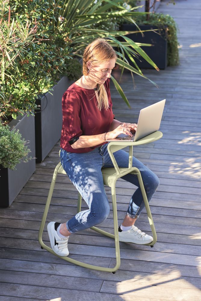 Frau arbeitet am Laptop auf dem Adadesk Beistelltisch Wippe von Fermob im Freien auf einer Terrasse.