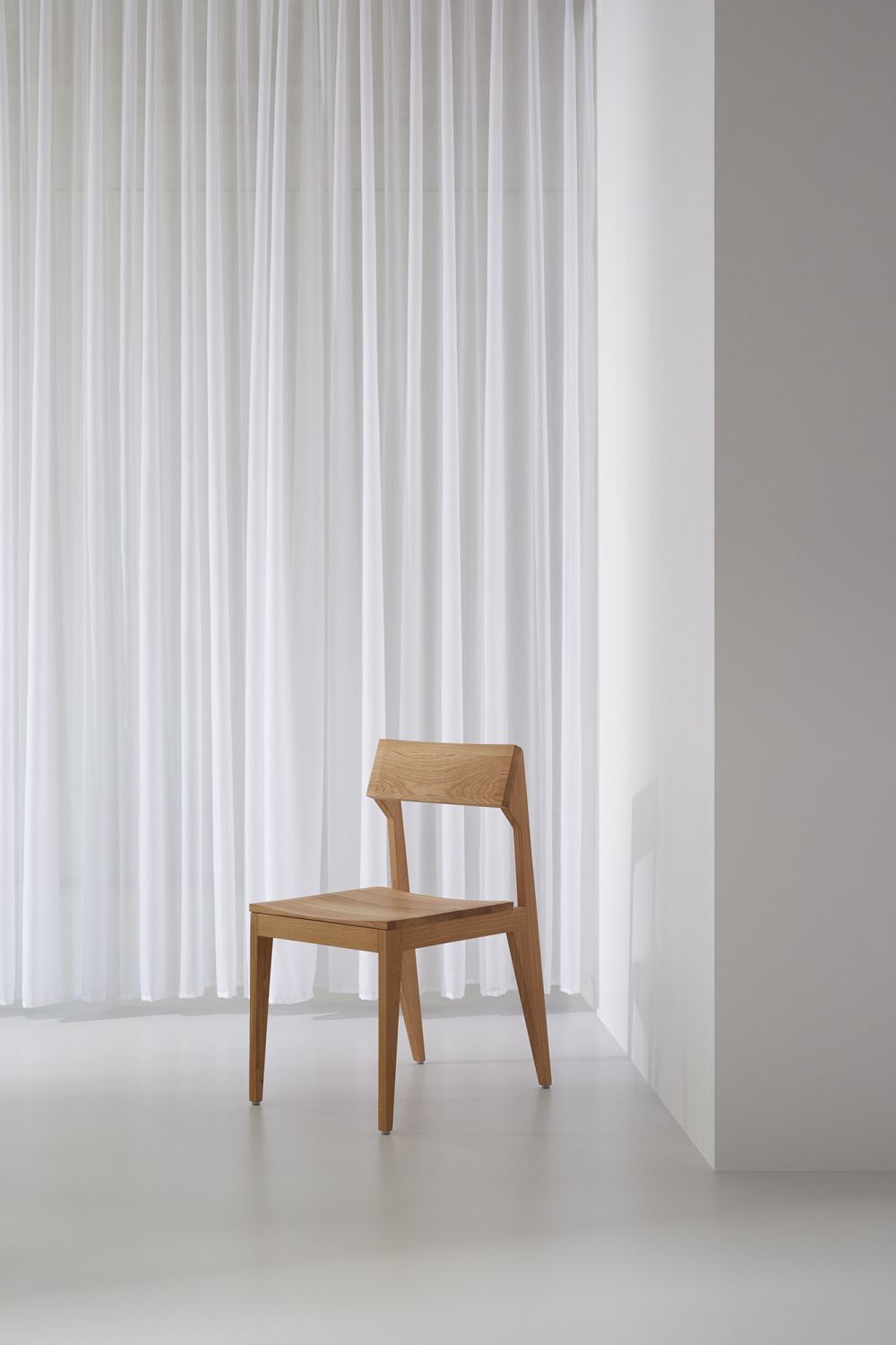 SCHULZ Stuhl aus hellem Holz vor weißem Vorhang und Wand, minimalistisches Design für Esszimmer und Wohnbereich.