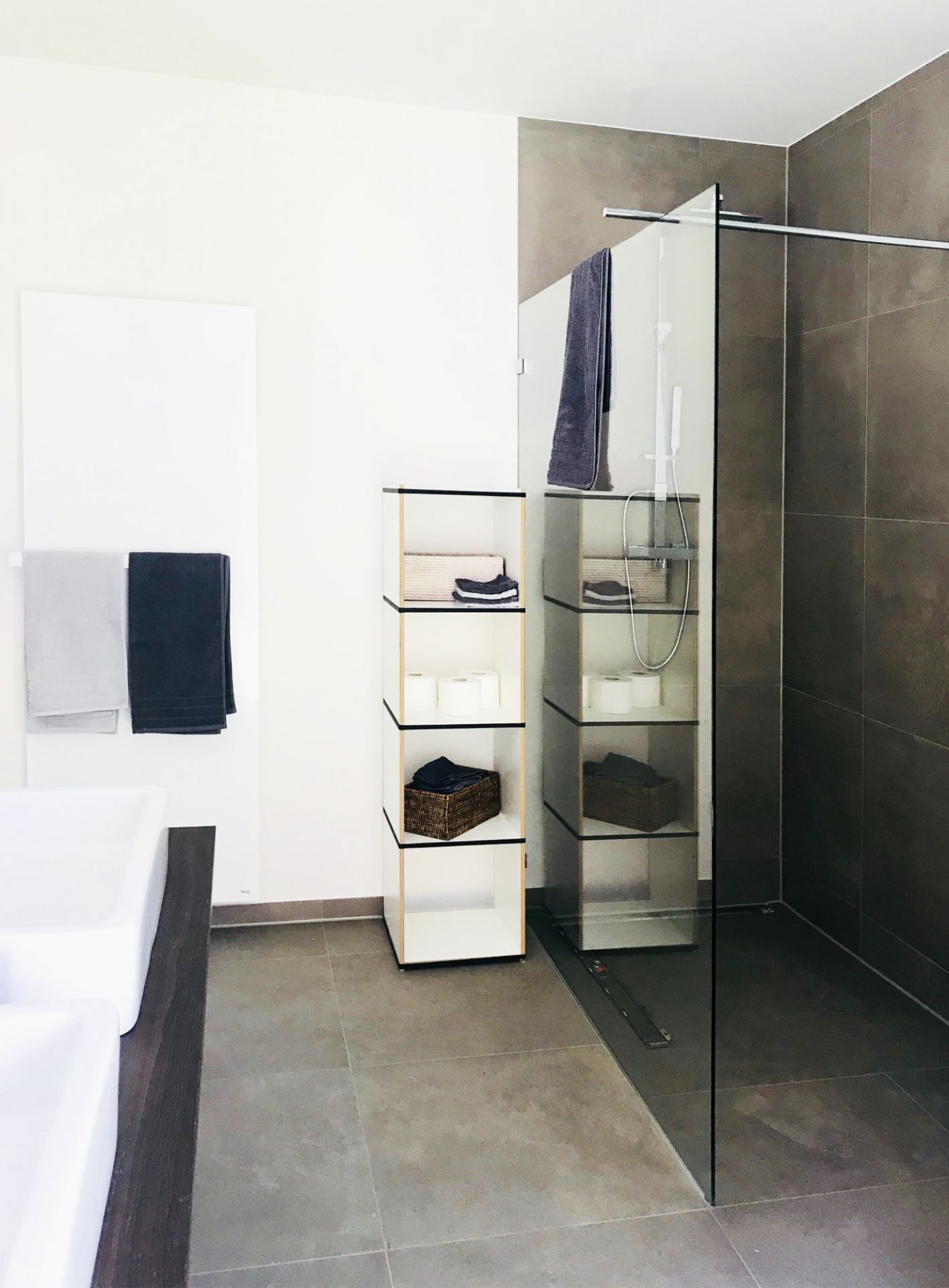 Badezimmer mit Tojo Regal Modul, weißem Waschtisch, Handtüchern und ebenerdiger Dusche für modernes Interior Design.