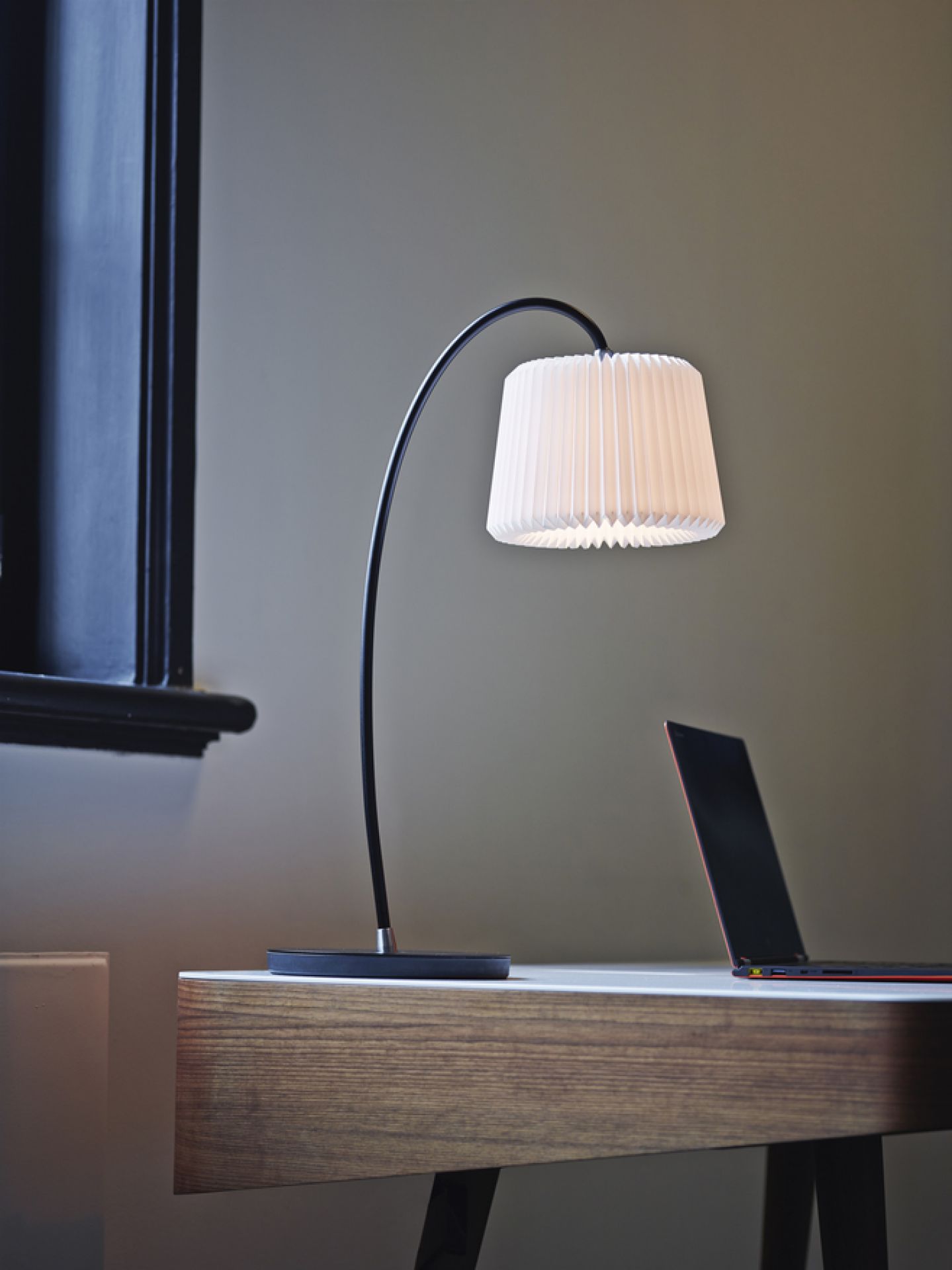 Snowdrop Tischleuchte von Le Klint auf einem Schreibtisch, mit plissiertem Lampenschirm und modernem Design.