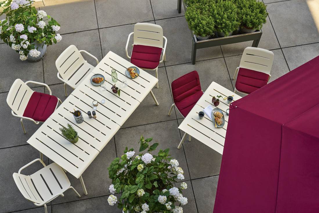Weishäupl Vapio Outdoor Tisch mit passenden Stühlen und burgunderroten Sitzkissen auf einer Terrasse.