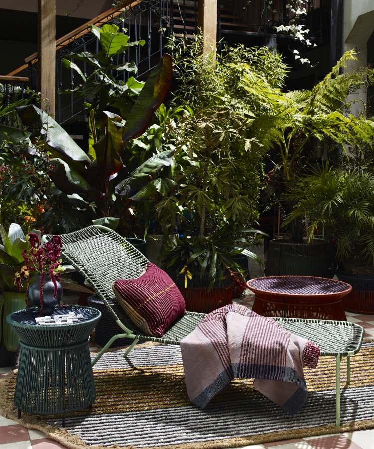 Moosgrüner Caribe Chic Beistelltisch Outdoor neben Liege mit Kissen und Decke im Garten.