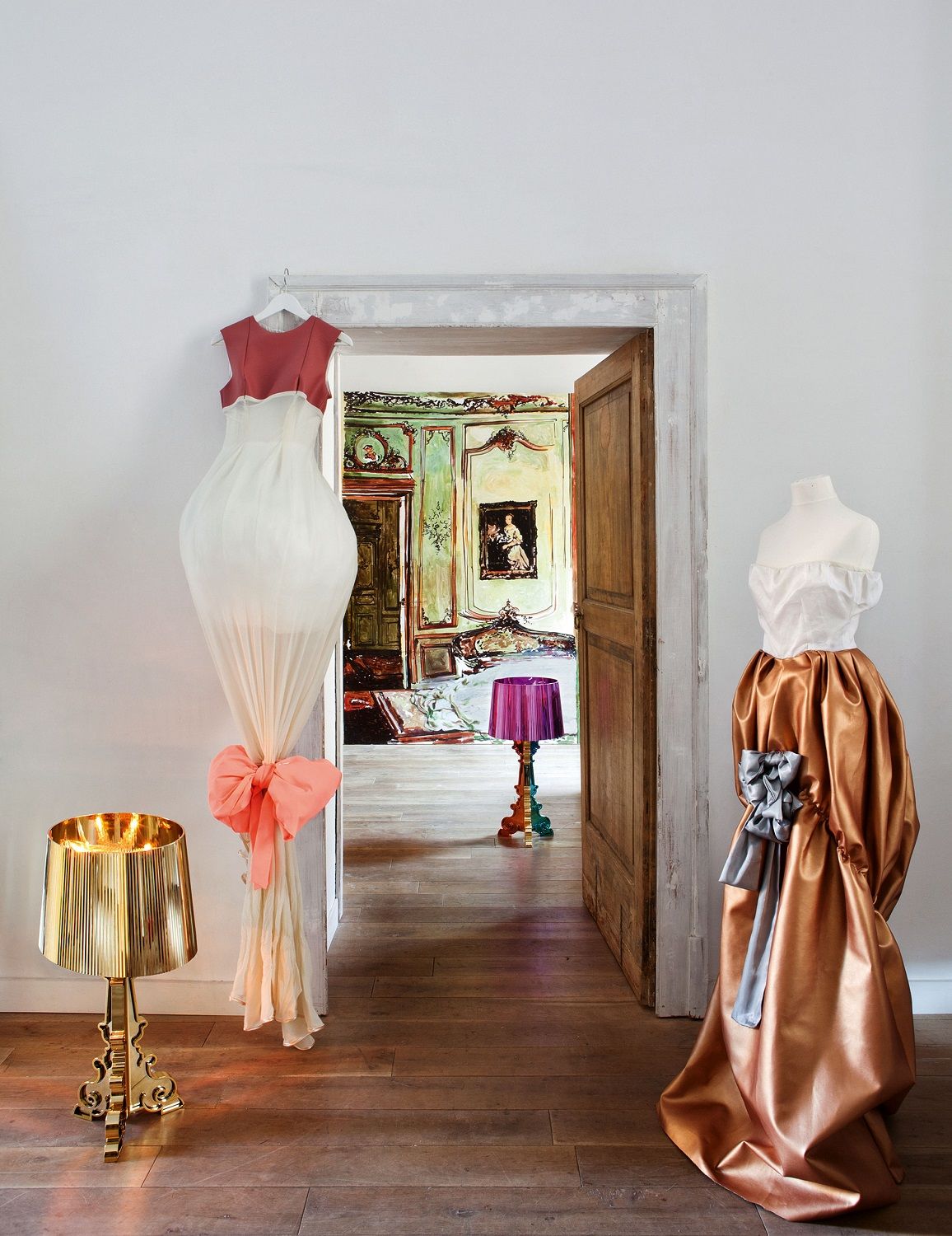 Dekoratives Interieur mit goldener Bourgie Tischleuchte von Kartell, Kleiderpuppen und Blick durch eine Tür in einen weiteren Raum.