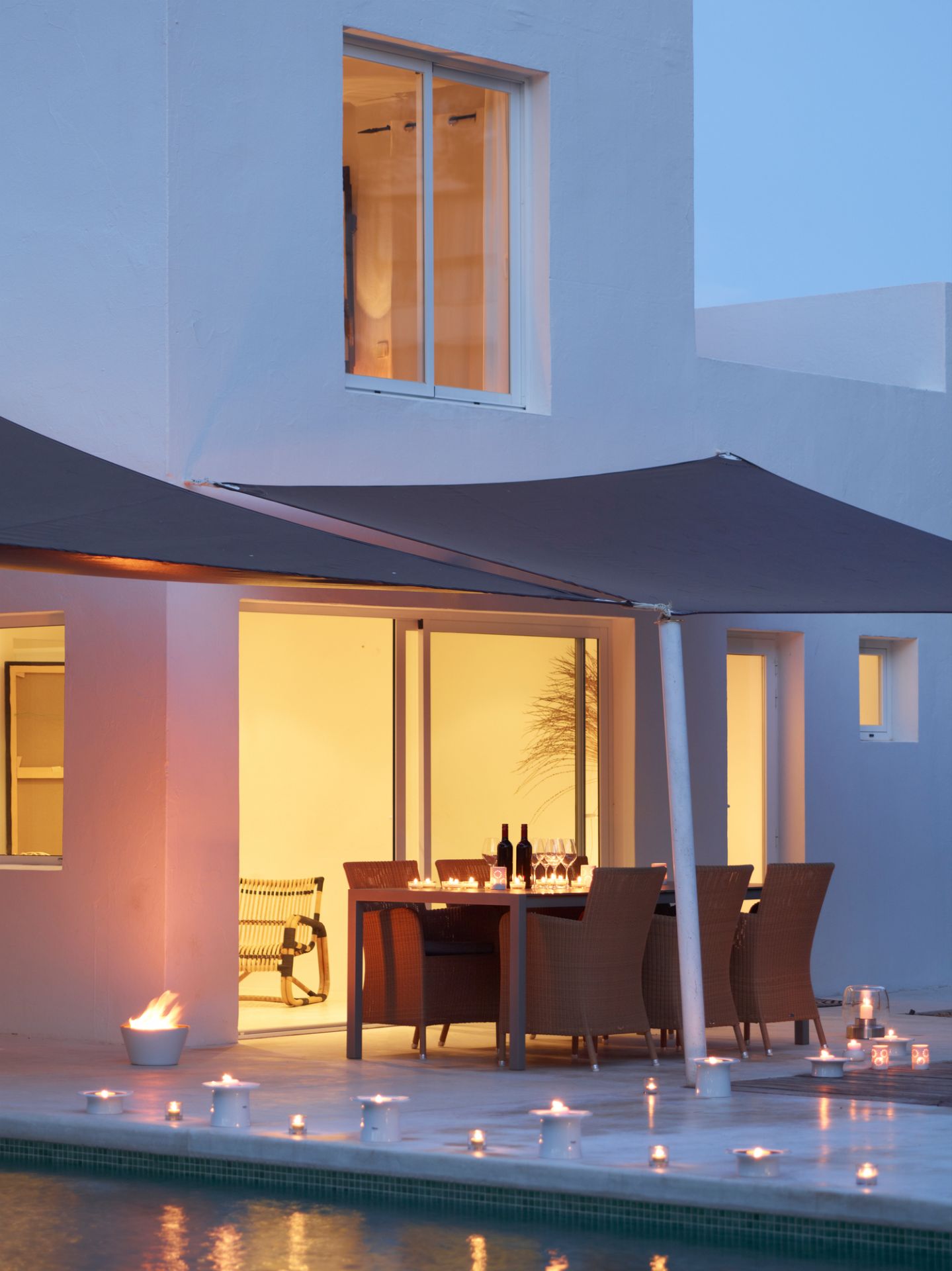 Hampsted Cane-Line Outdoor Sessel aus Rattan auf Terrasse mit Esstisch und Pool bei Nacht.