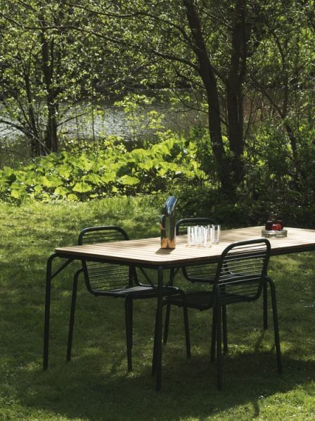 Normann Copenhagen Vig Table Outdoor mit Stühlen im Garten, gedeckt mit Gläsern und Getränkekaraffe.