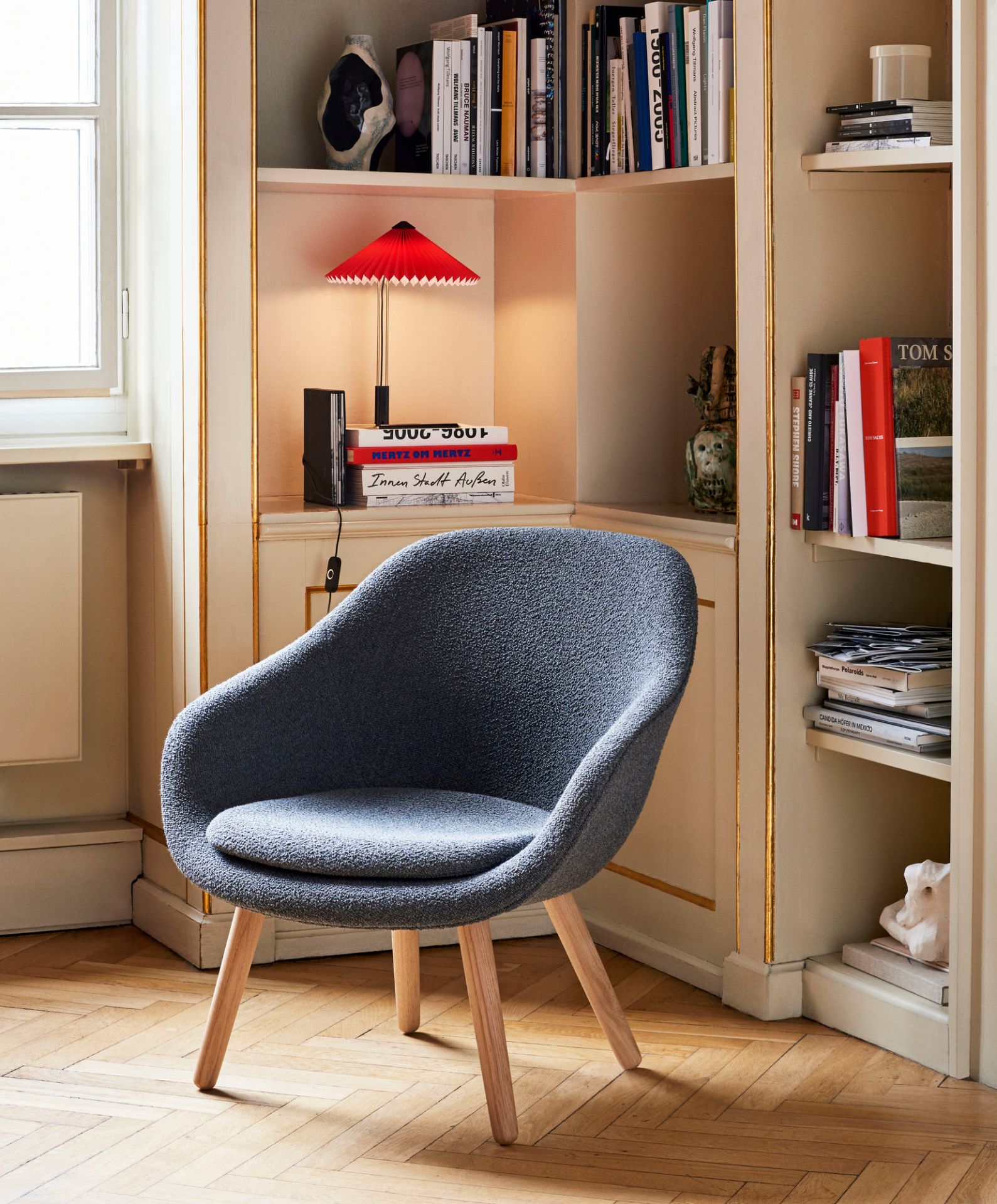 Blauer About a Lounge Sessel (AAL 82) von Hay mit Holzbeinen vor Bücherregal.