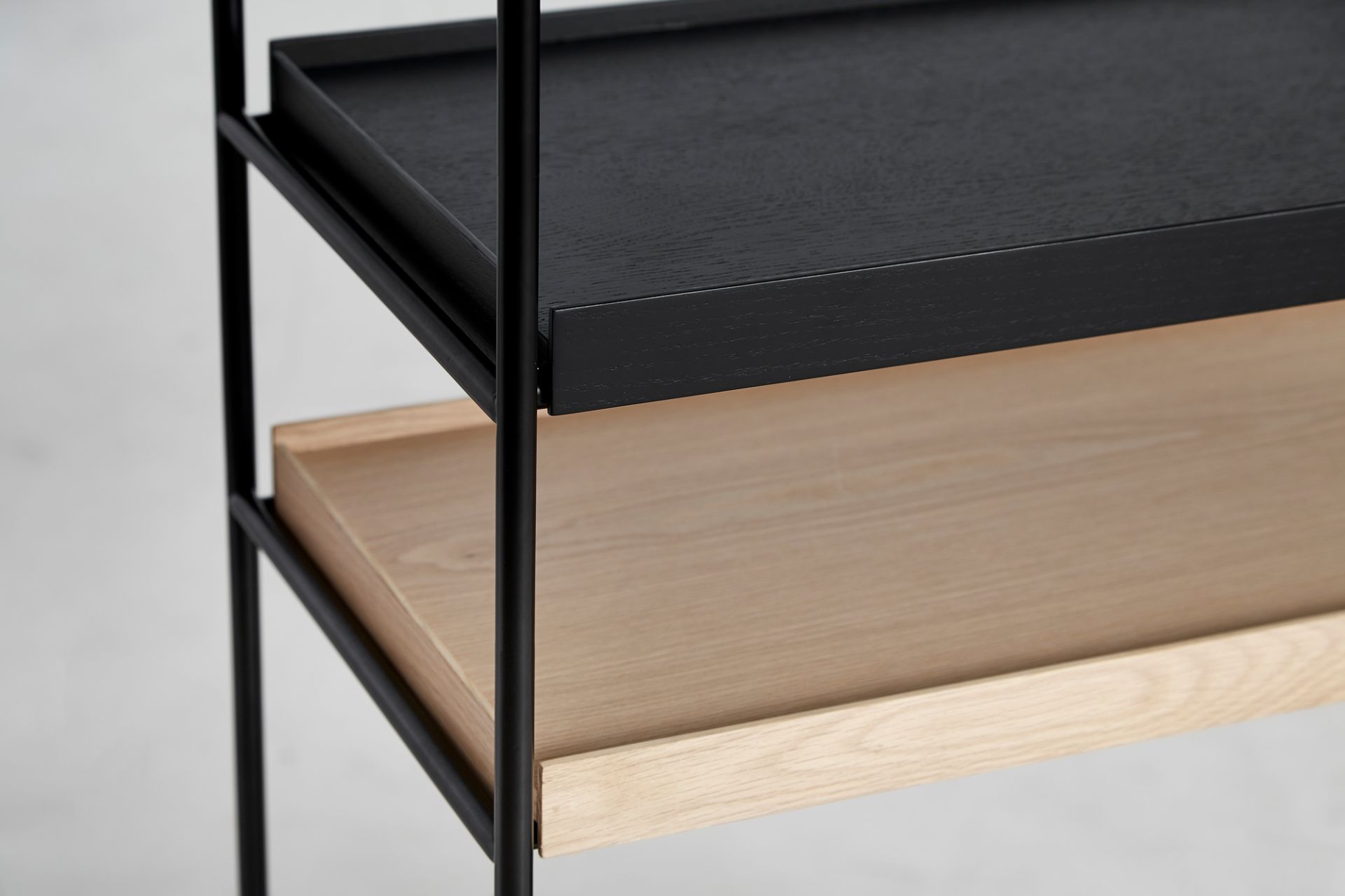 Detailaufnahme des Woud Tray Shelf Low Regals mit schwarzen und hellen Holztabletts und schwarzem Metallrahmen.