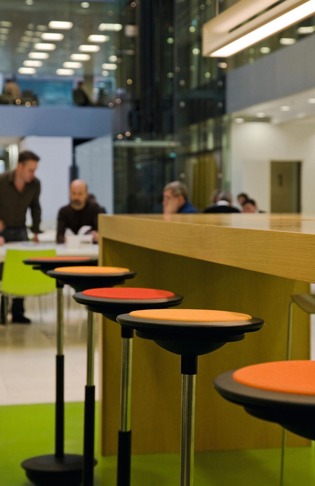Wilkhahn Stitz Stehhocker in Orange und Rot vor einer Theke in einem Büro.