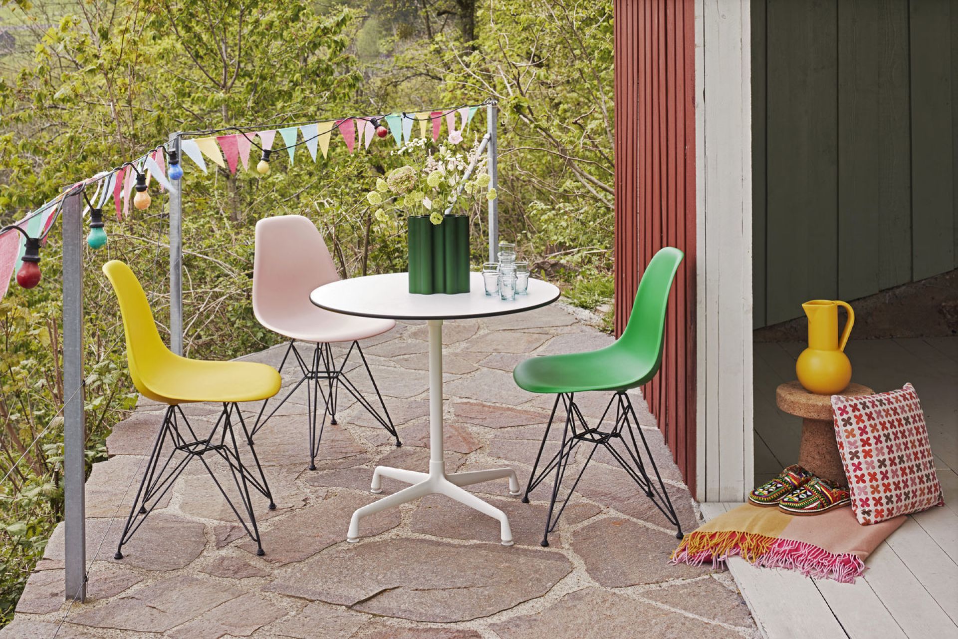 Drei Eames Plastic Side Chairs DSR von Vitra in Gelb, Rosa und Grün an einem Gartentisch.