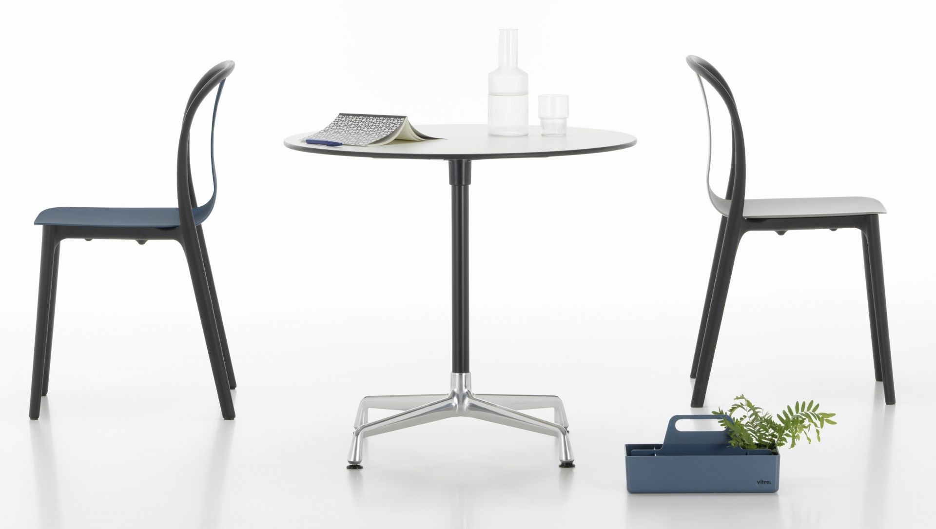 Eames Contract Table von Vitra mit zwei Stühlen, Wasserflasche und Notizblock auf weißem Hintergrund.