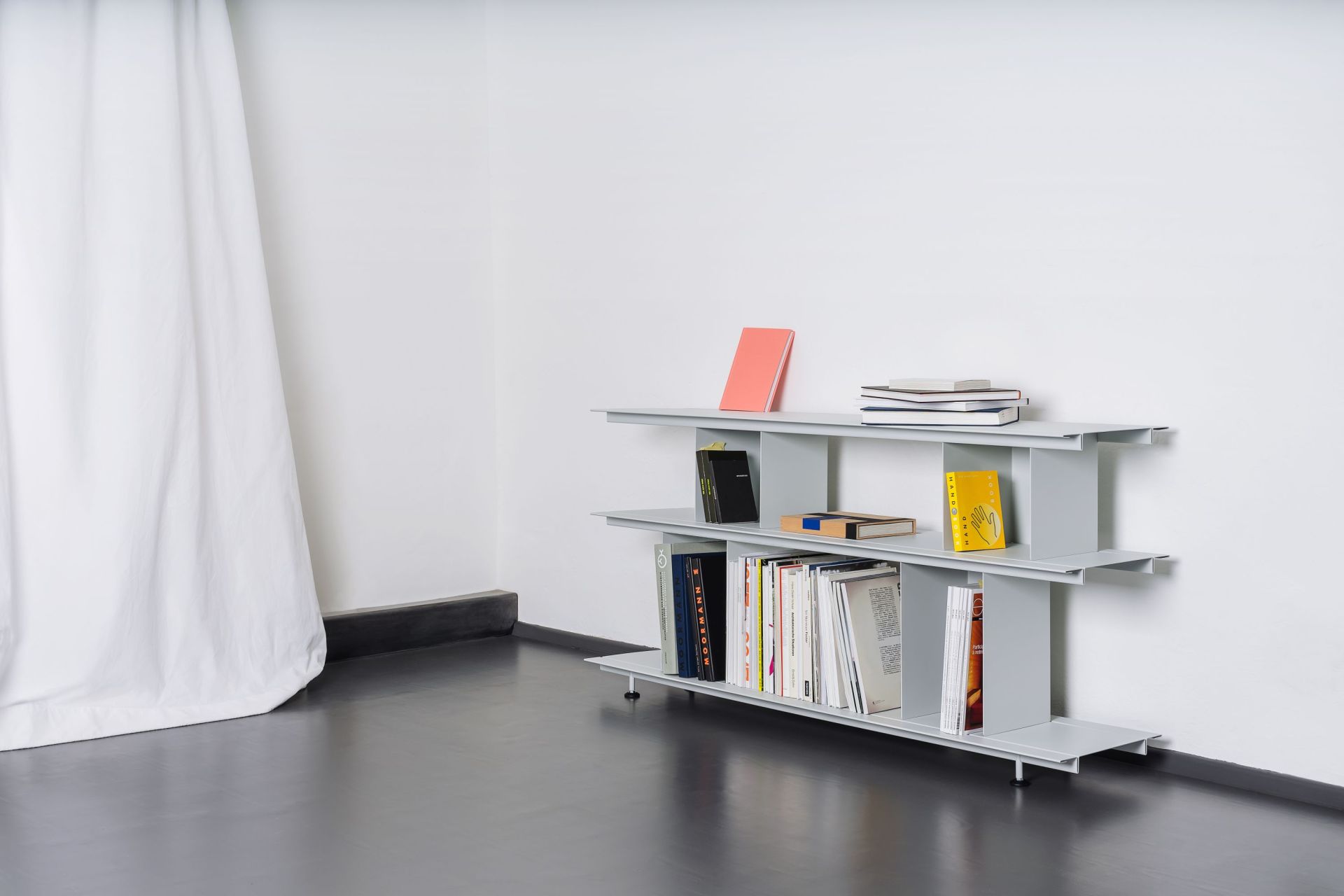 Graues Zoll D Regal von Nils Holger Moormann mit Büchern vor weißer Wand und Vorhang.